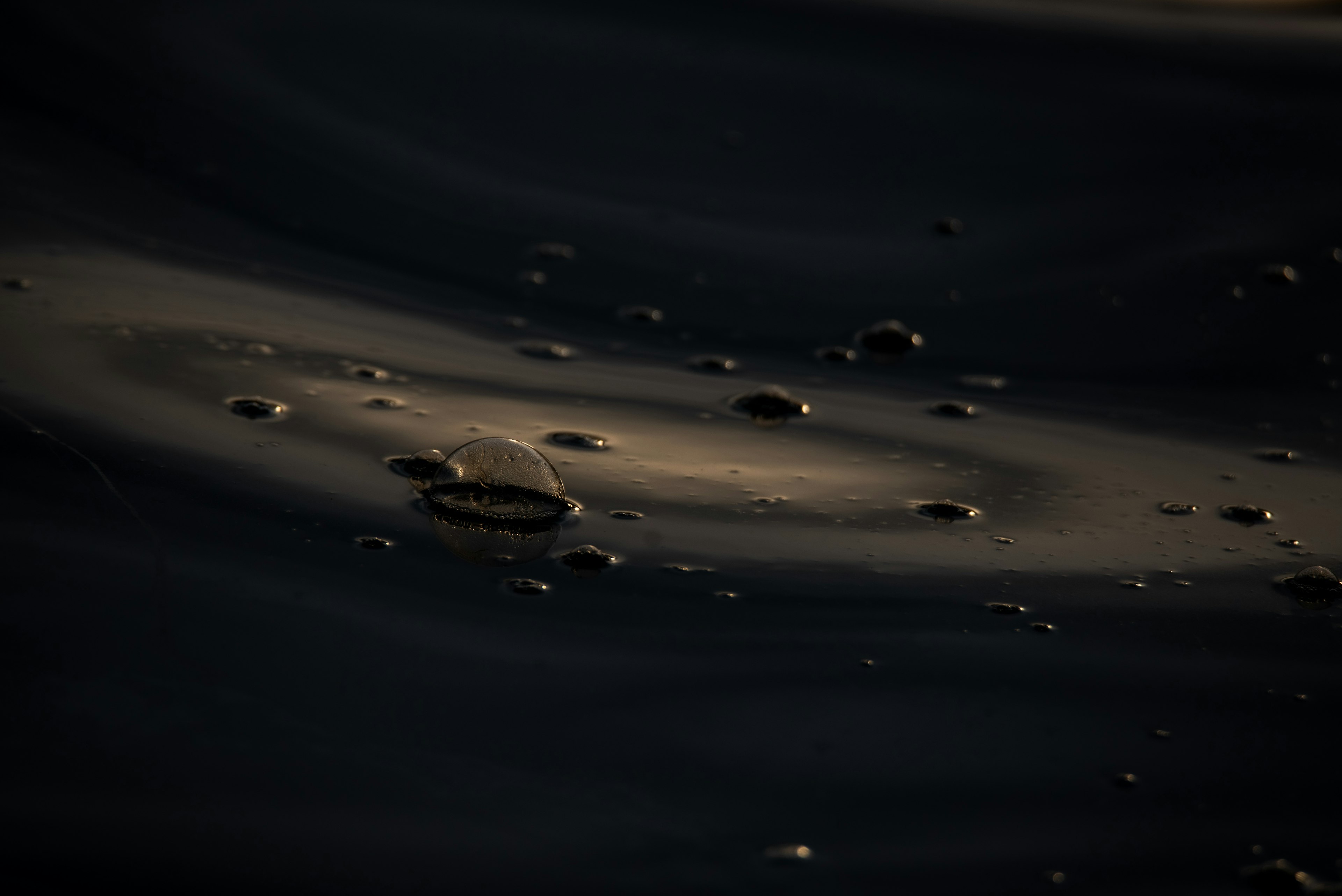 Small water droplets floating on a dark surface with light reflections