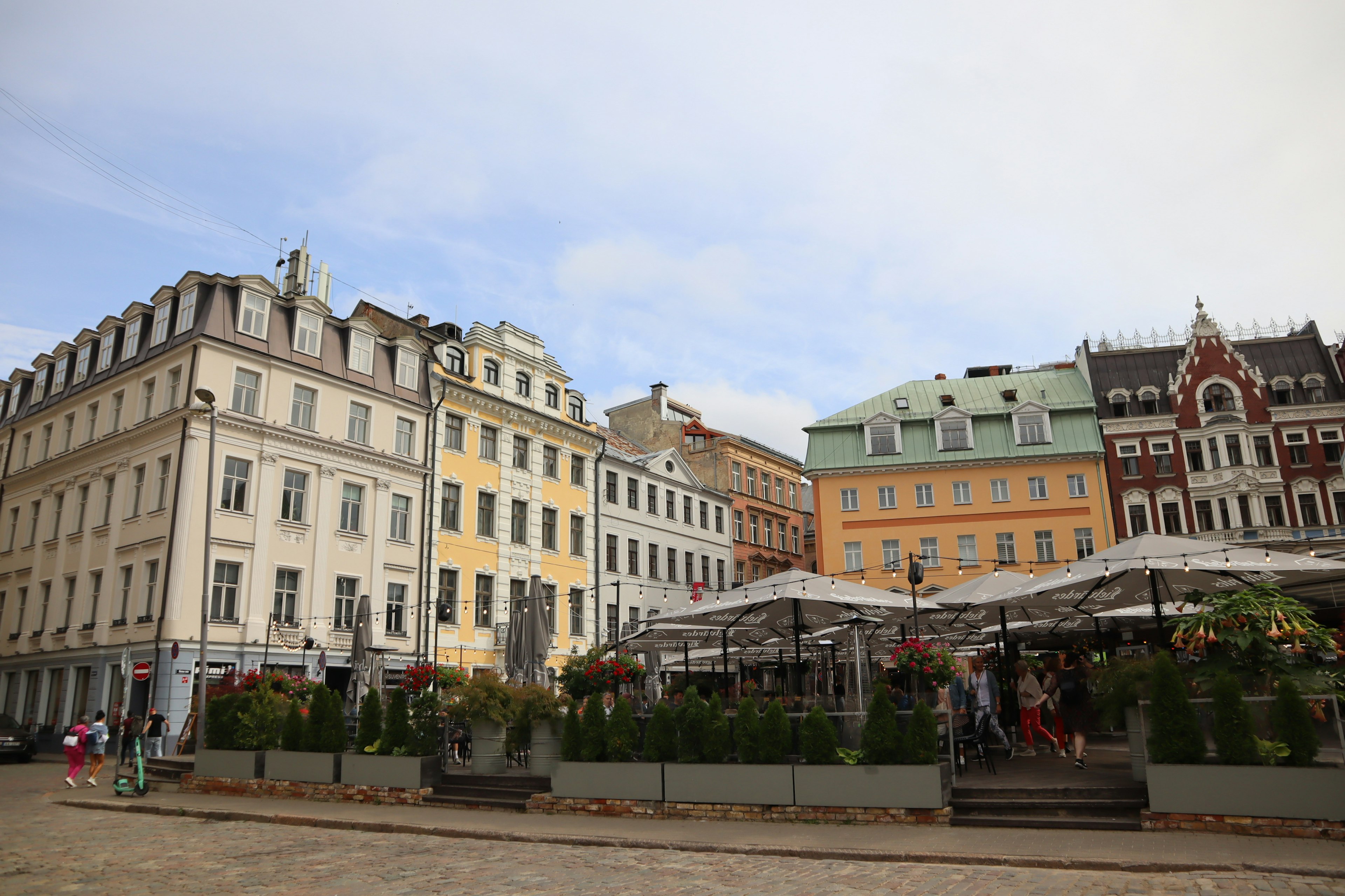 Bâtiments colorés bordant une place avec une terrasse de café et des décorations florales