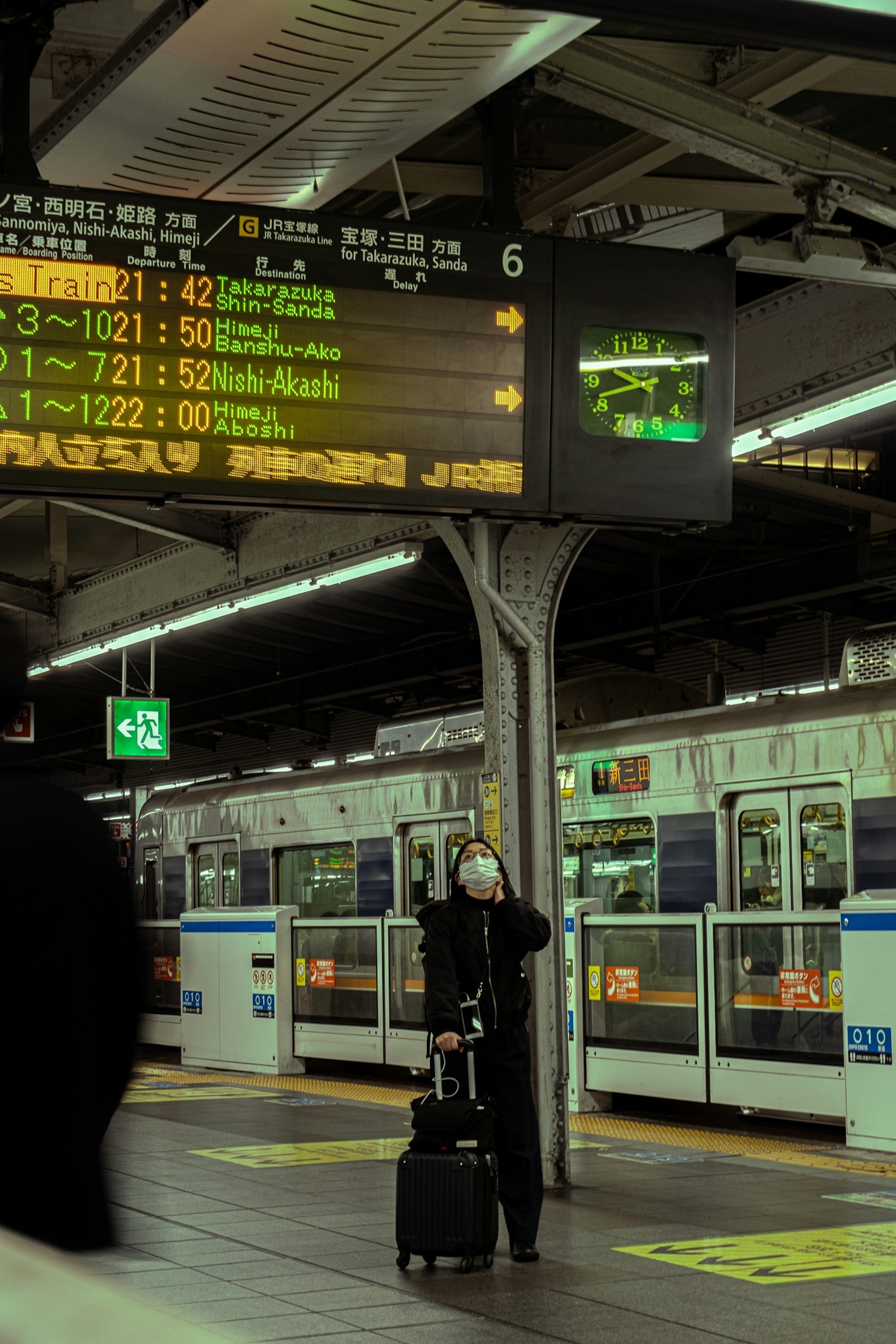 Une personne attendant sur un quai de train avec un tableau d'affichage numérique