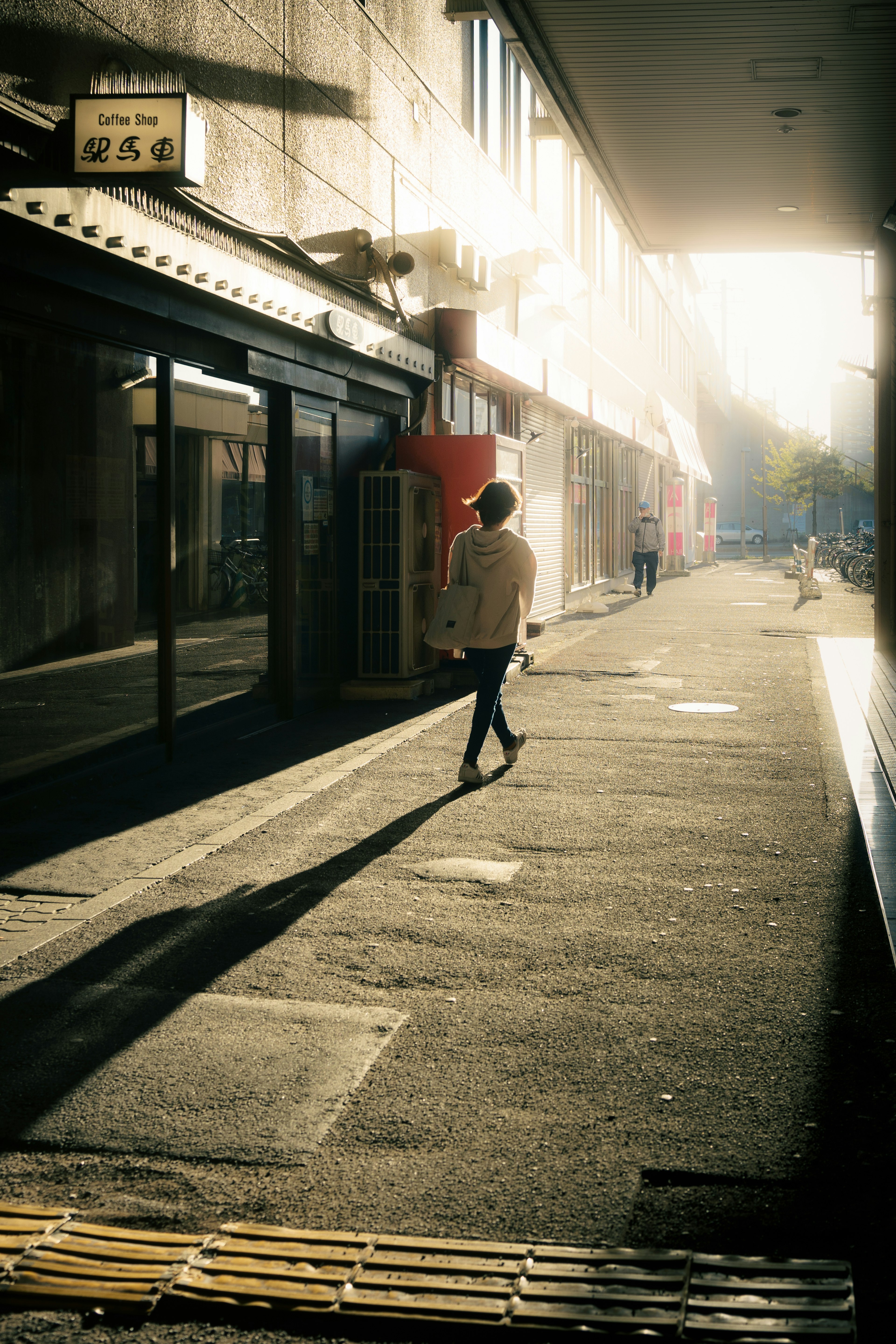 Una persona che cammina in una strada poco illuminata con ombre e luce solare contrastanti