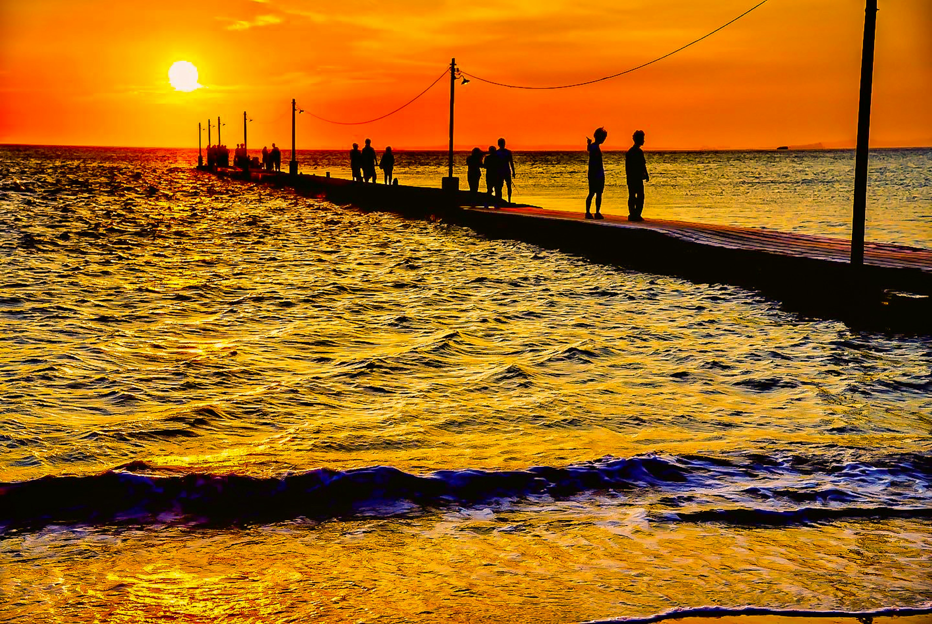 Silhouettes of people on a pier against a sunset