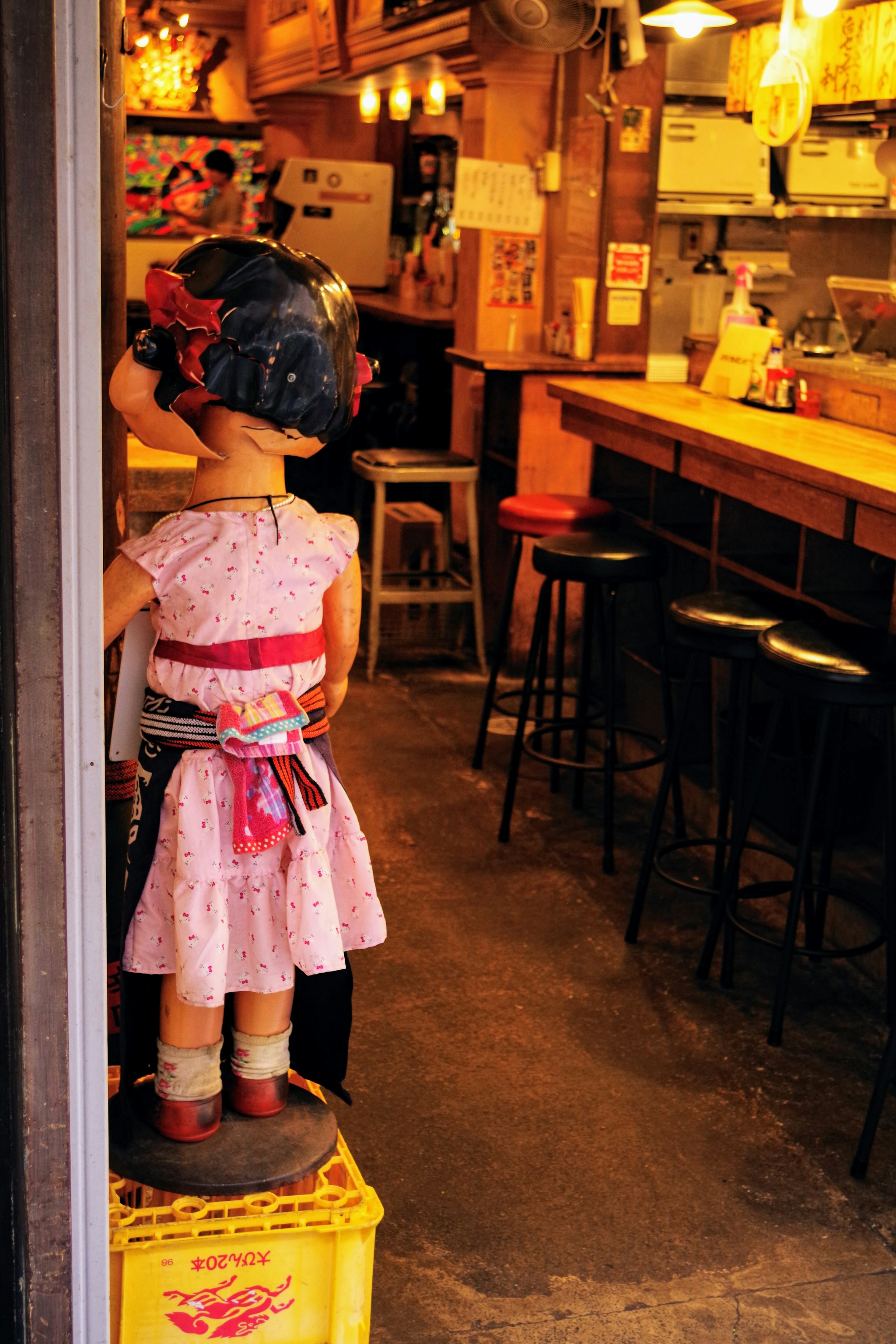 Una pequeña muñeca de niña con vestido rosa está en el interior de un izakaya acogedor