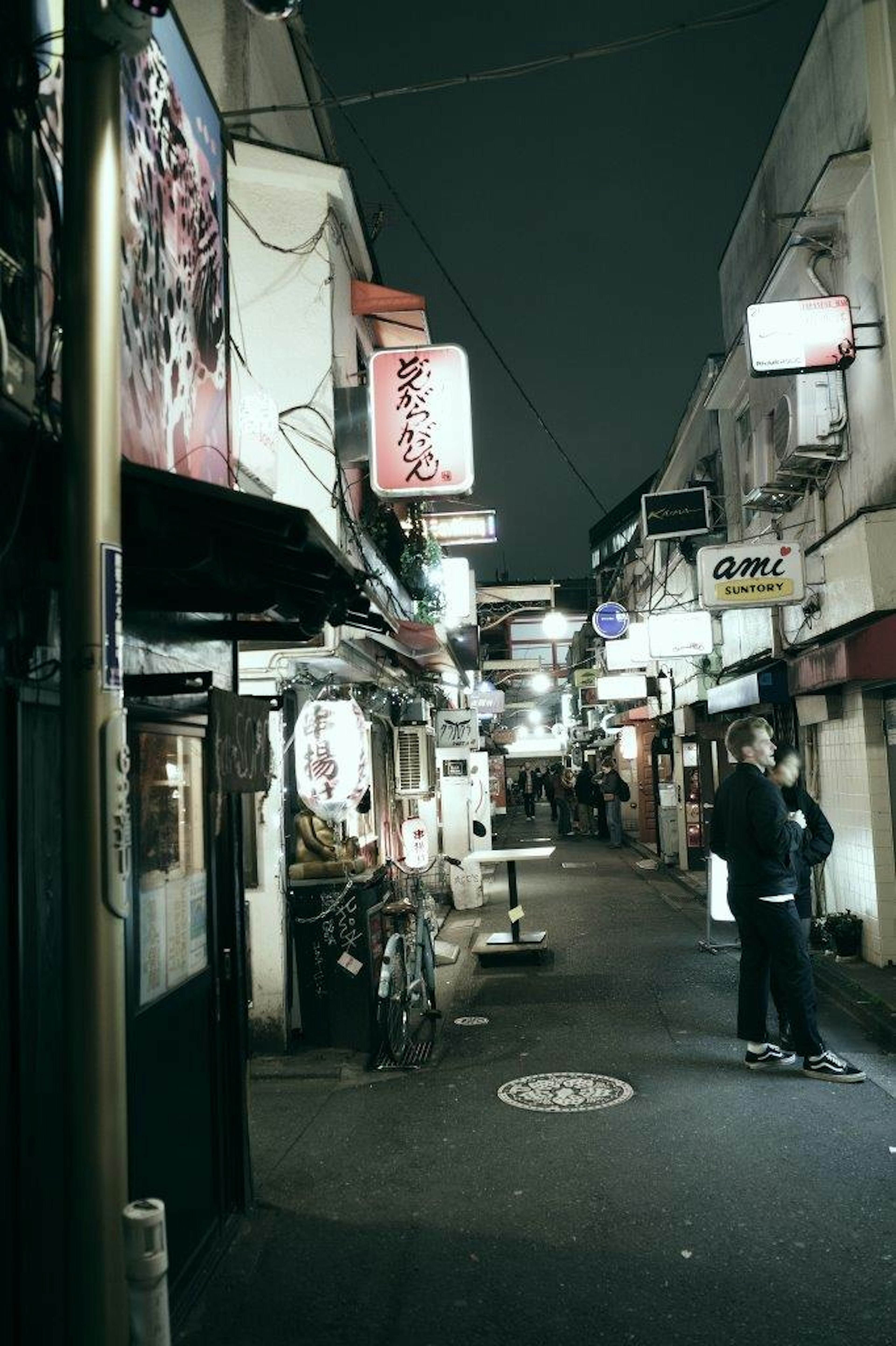 夜の狭い通りに並ぶ飲食店の看板と人影