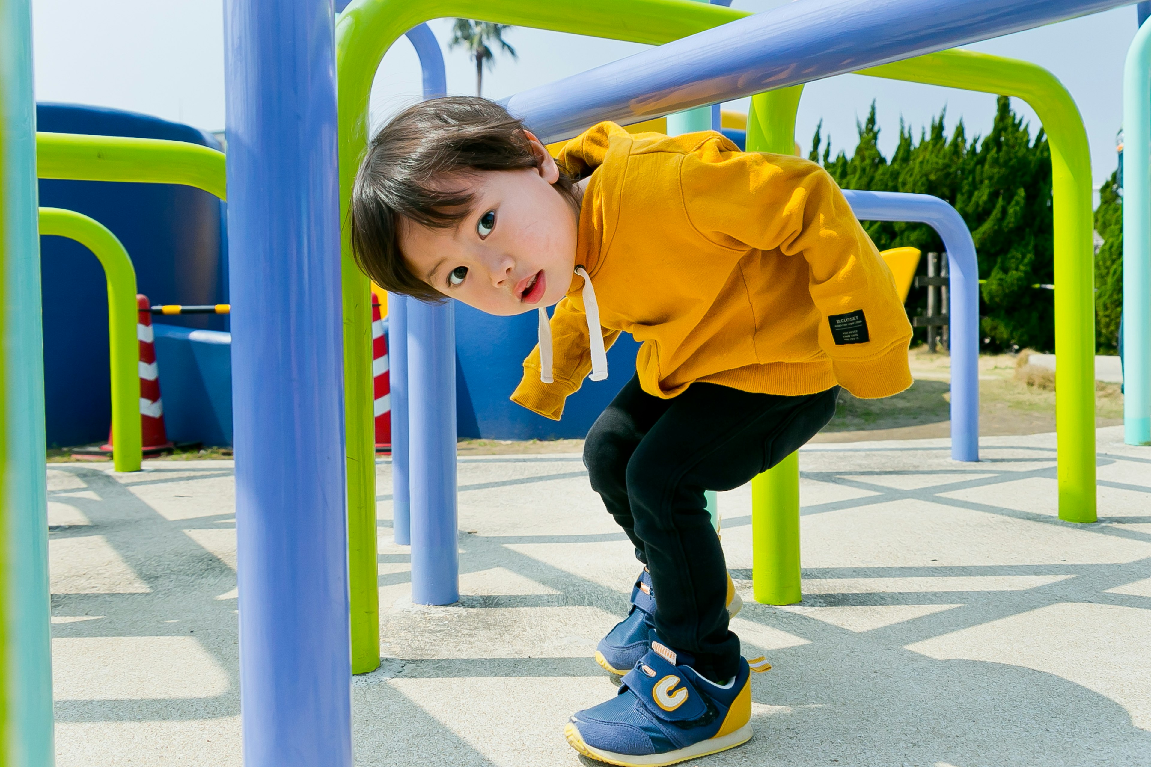 Seorang anak bermain di taman merangkak di bawah peralatan bermain berwarna