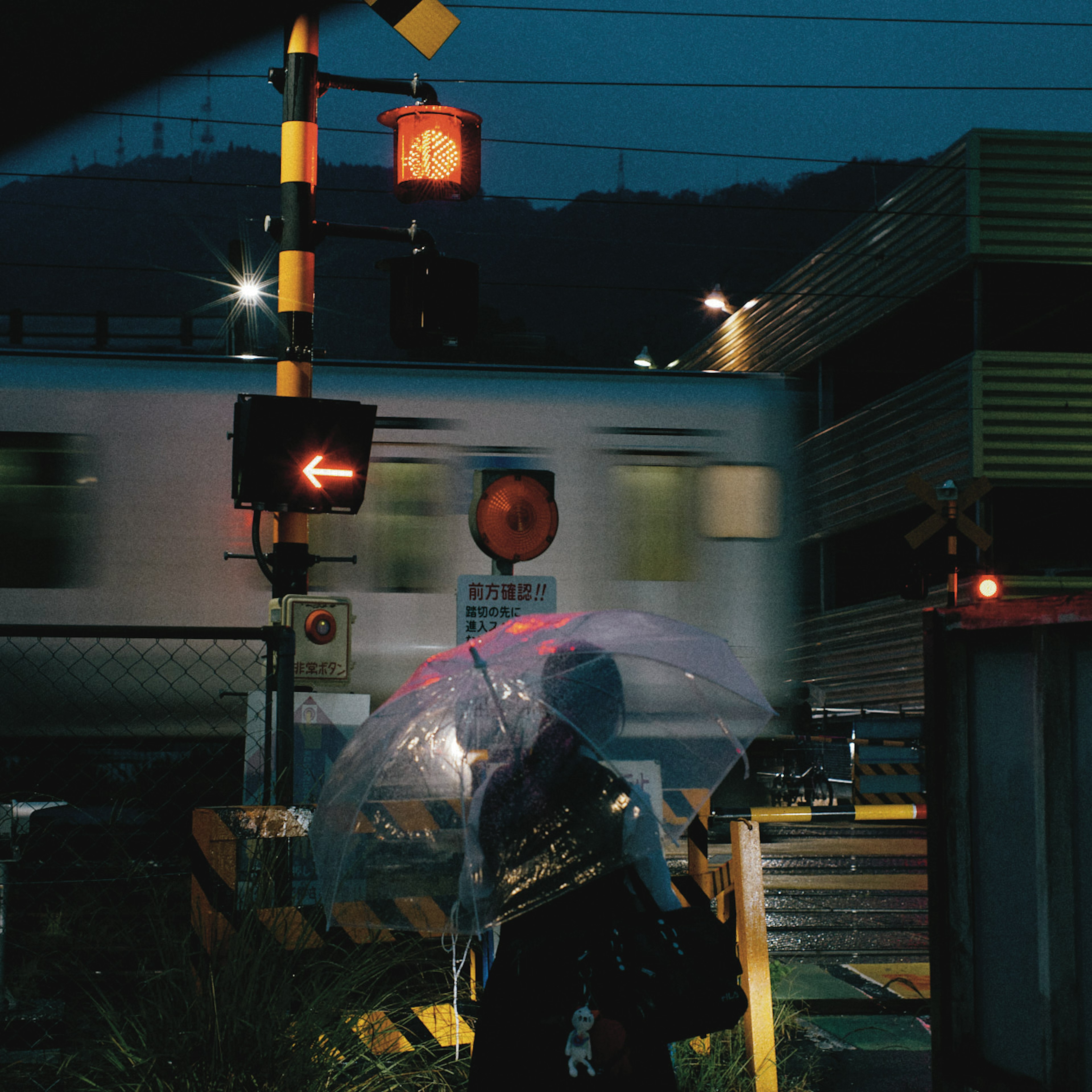 夜の駅で傘を持った人物が列車の通過を待っている風景