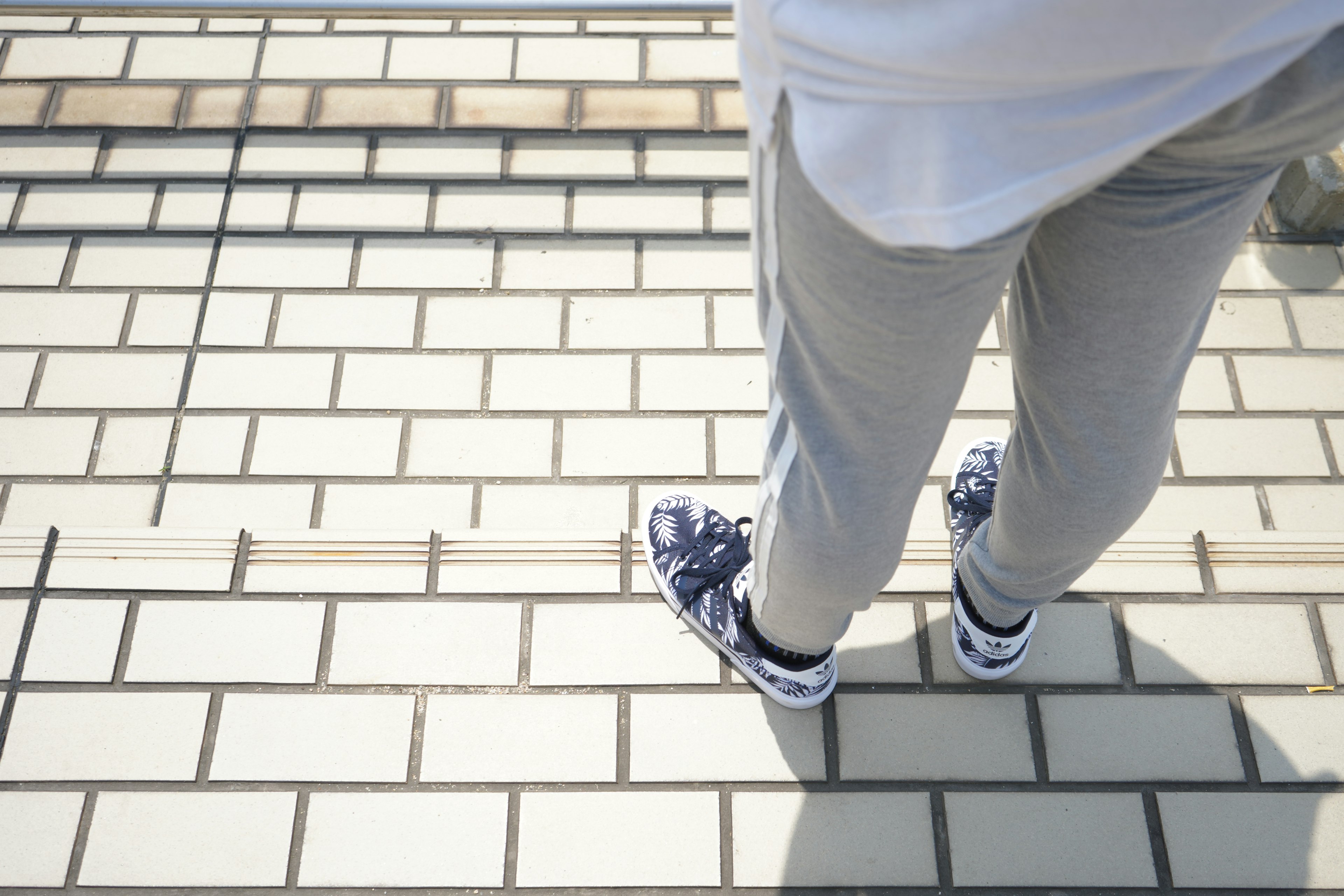 Person wearing white t-shirt and gray pants walking on tiled surface