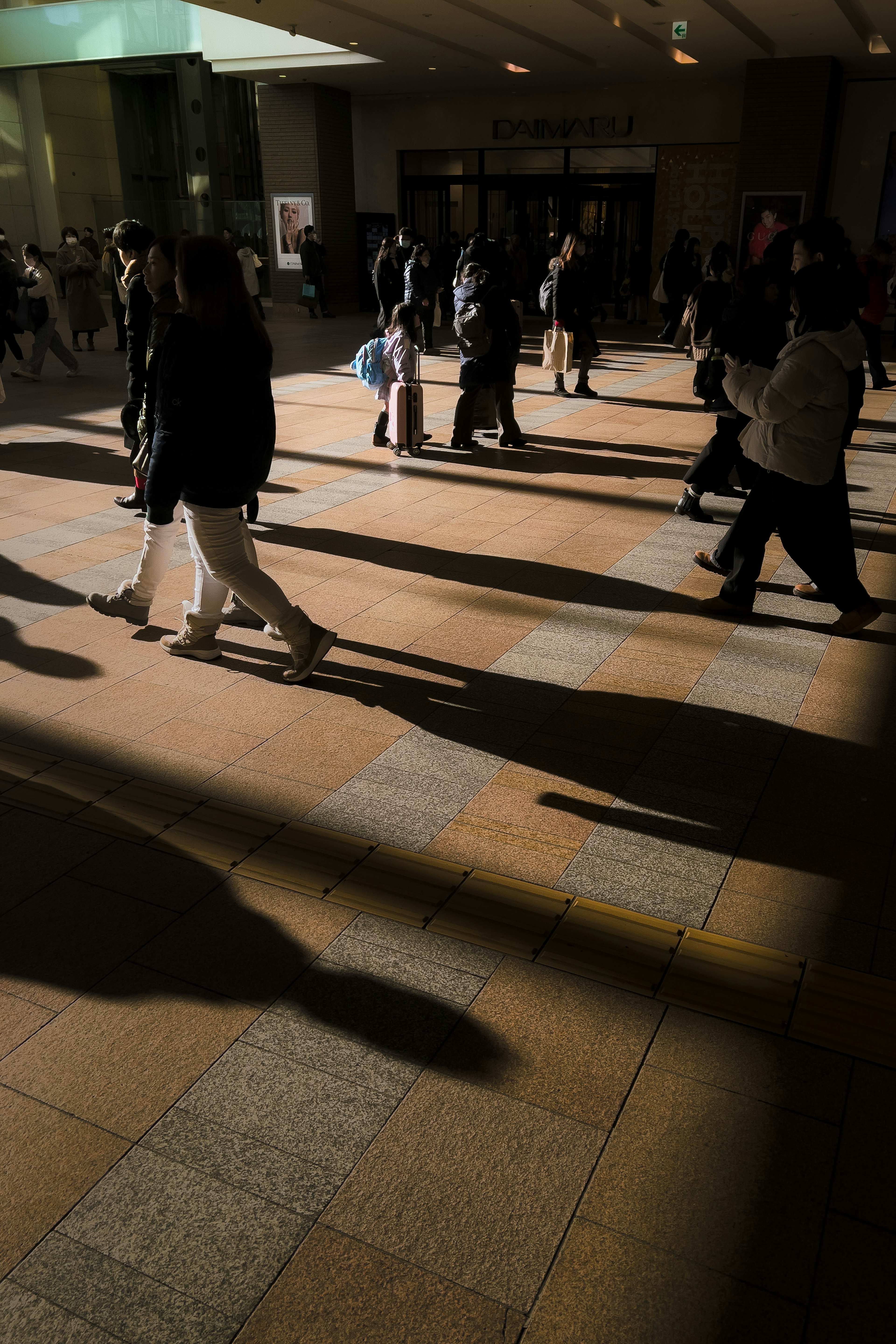 Personas caminando con largas sombras en un espacio comercial