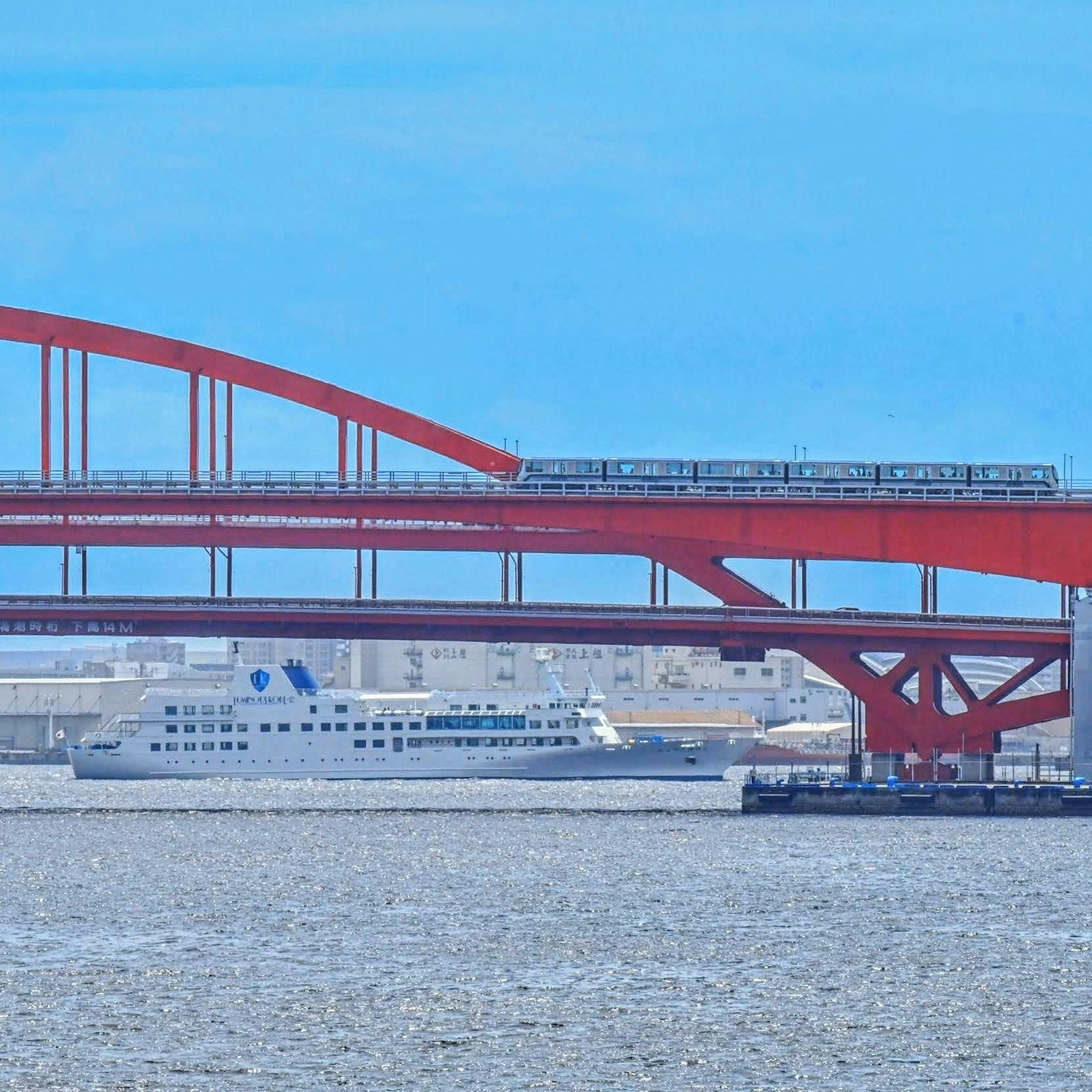 Jembatan lengkung merah dengan kapal di bawah langit biru cerah