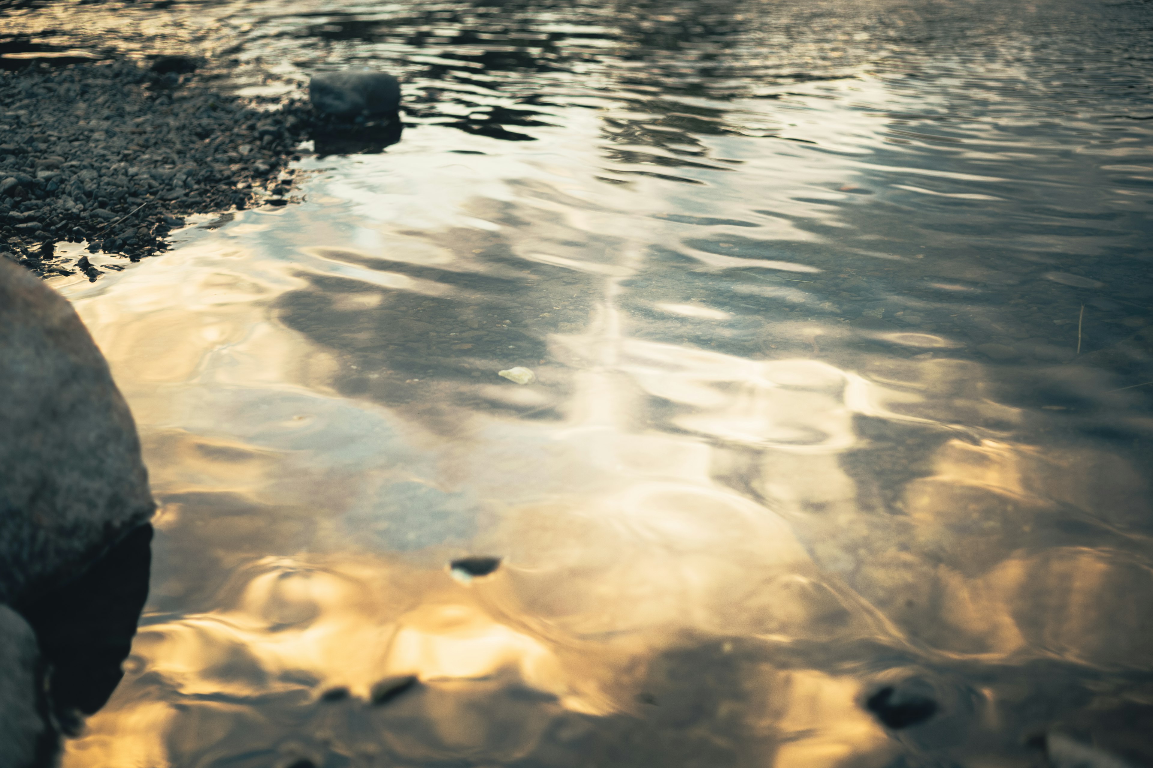 Serene water surface reflecting golden hues and surrounding rocks