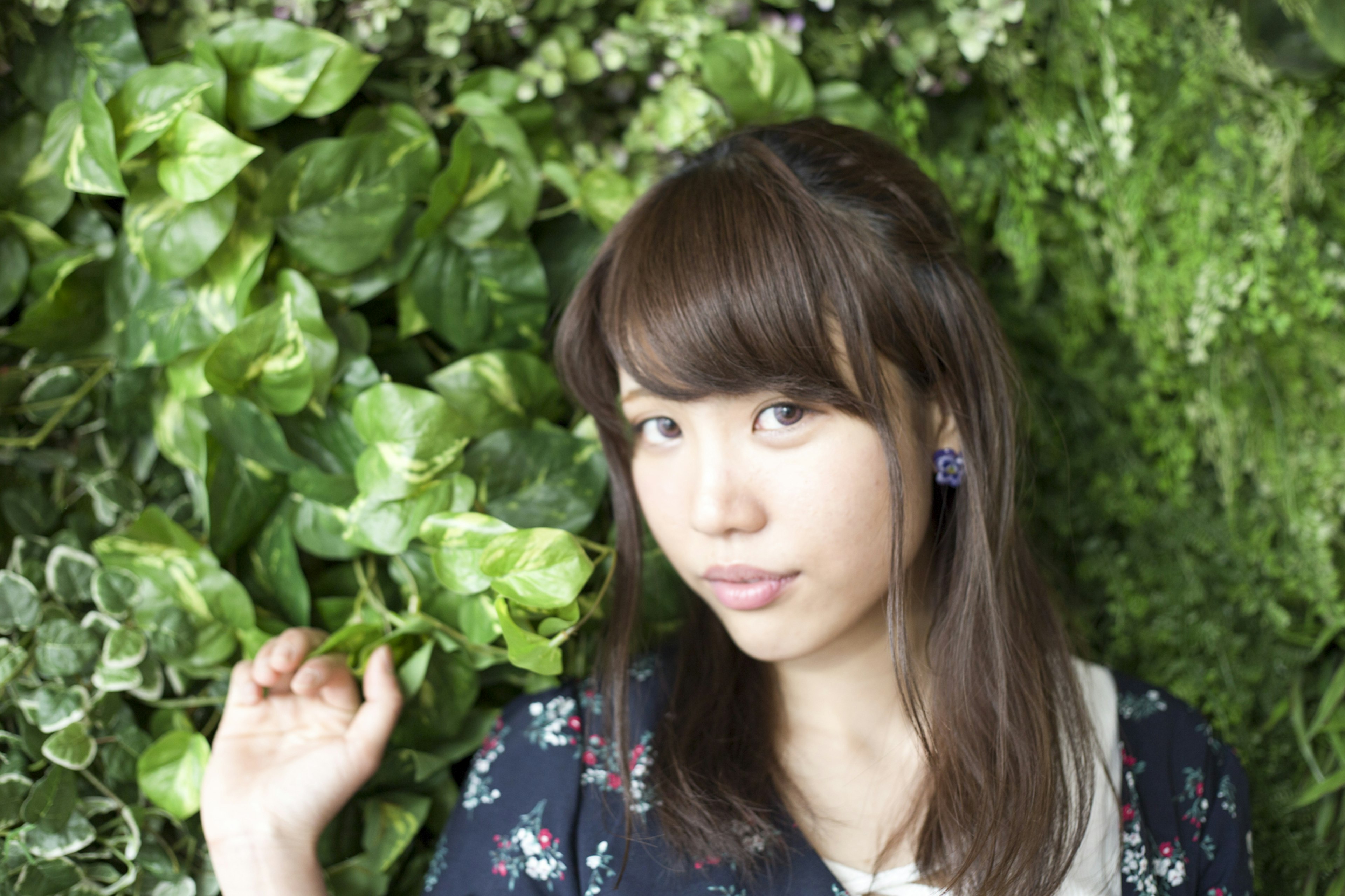 Portrait d'une femme devant un mur de plantes vertes