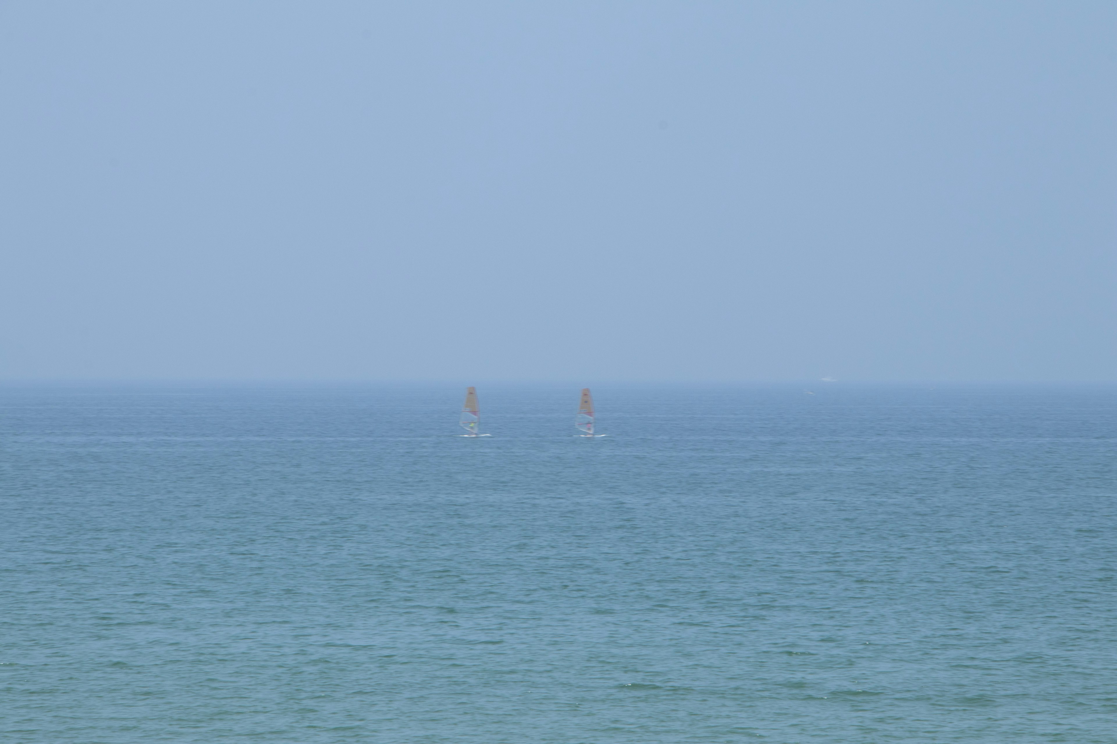 Two sailboats in the distance on a blue sea with a hazy sky