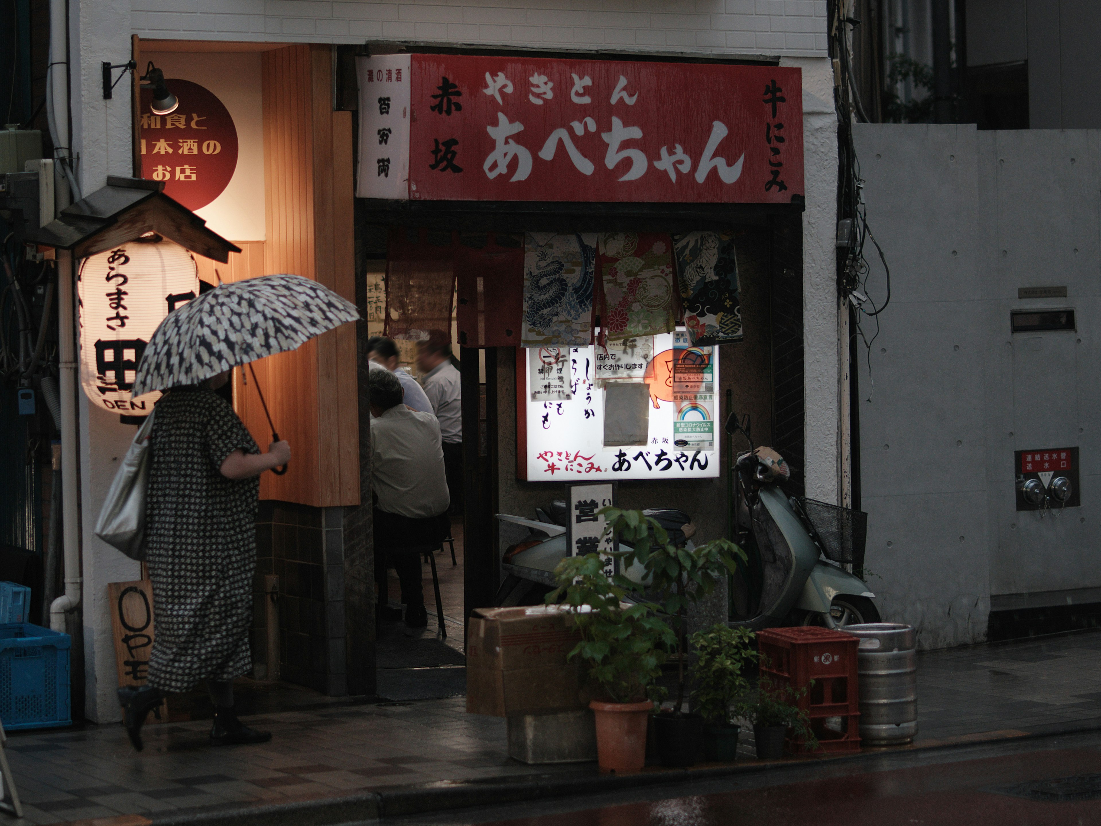 Exterior of a small eatery in the rain person holding an umbrella red sign with Japanese characters