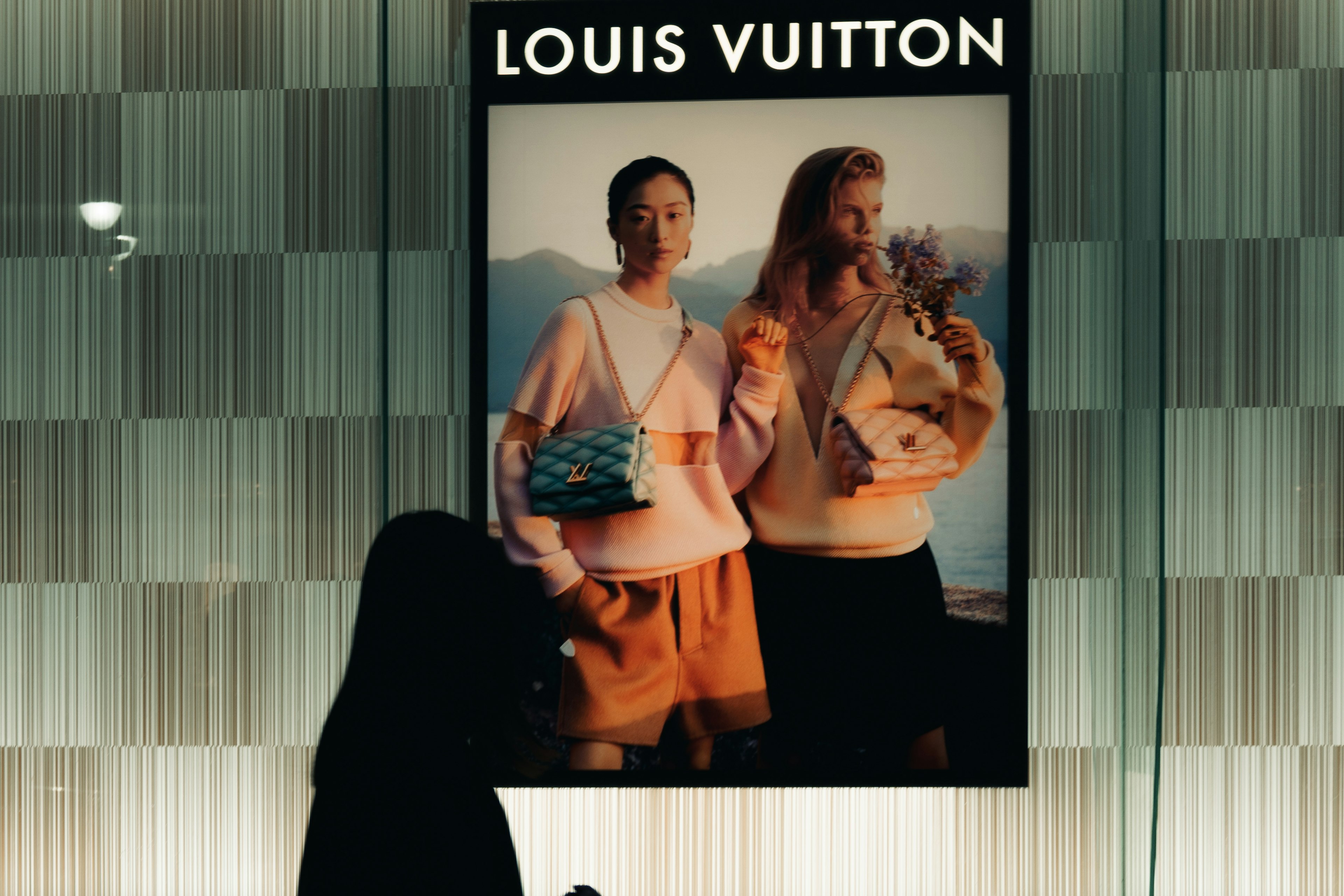 Silhouette d'une personne devant une publicité Louis Vuitton avec deux modèles