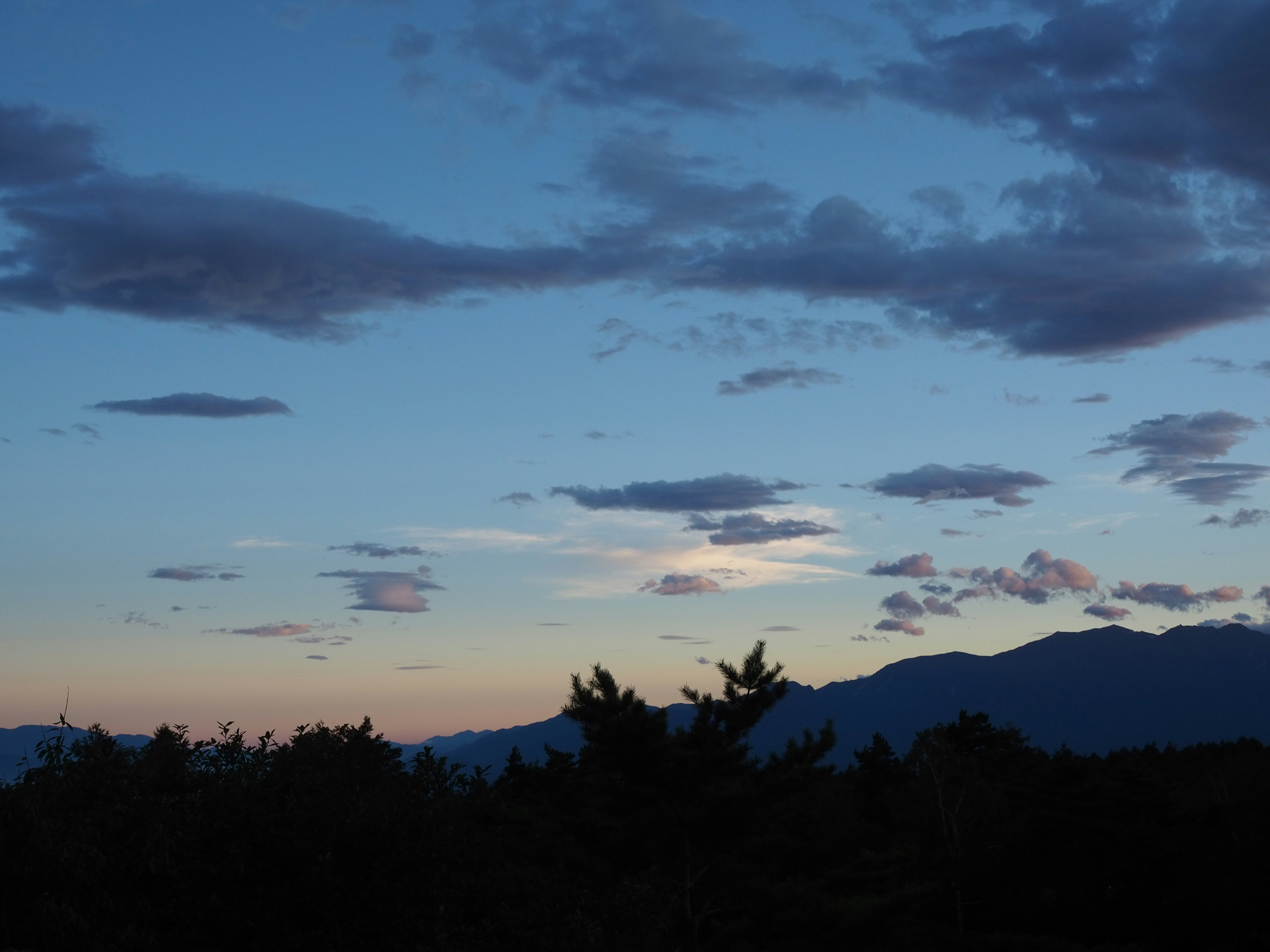 Langit senja dengan nuansa biru dan awan tersebar siluet gunung terlihat