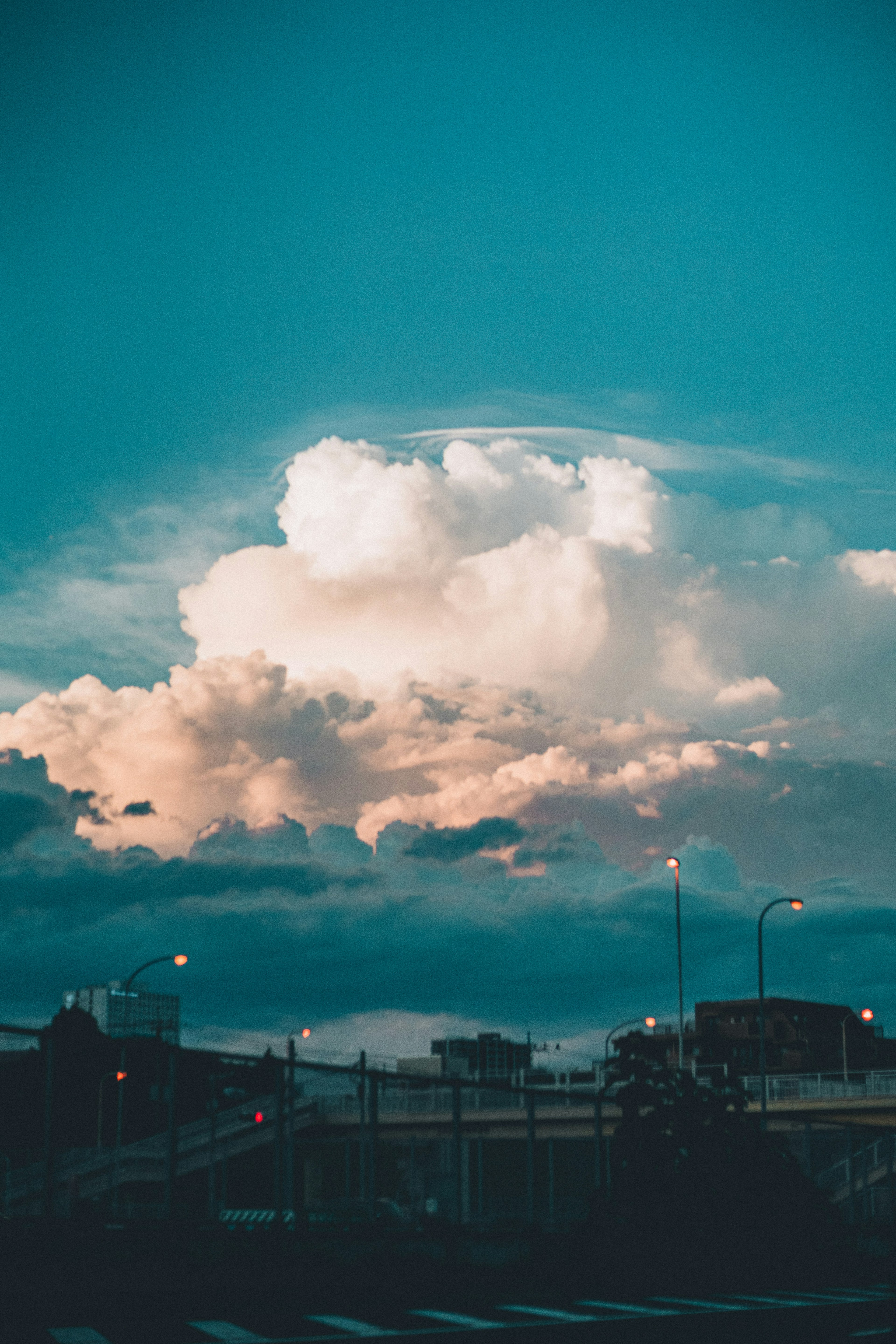 Awan besar melayang di langit biru dengan pemandangan kota di bawah