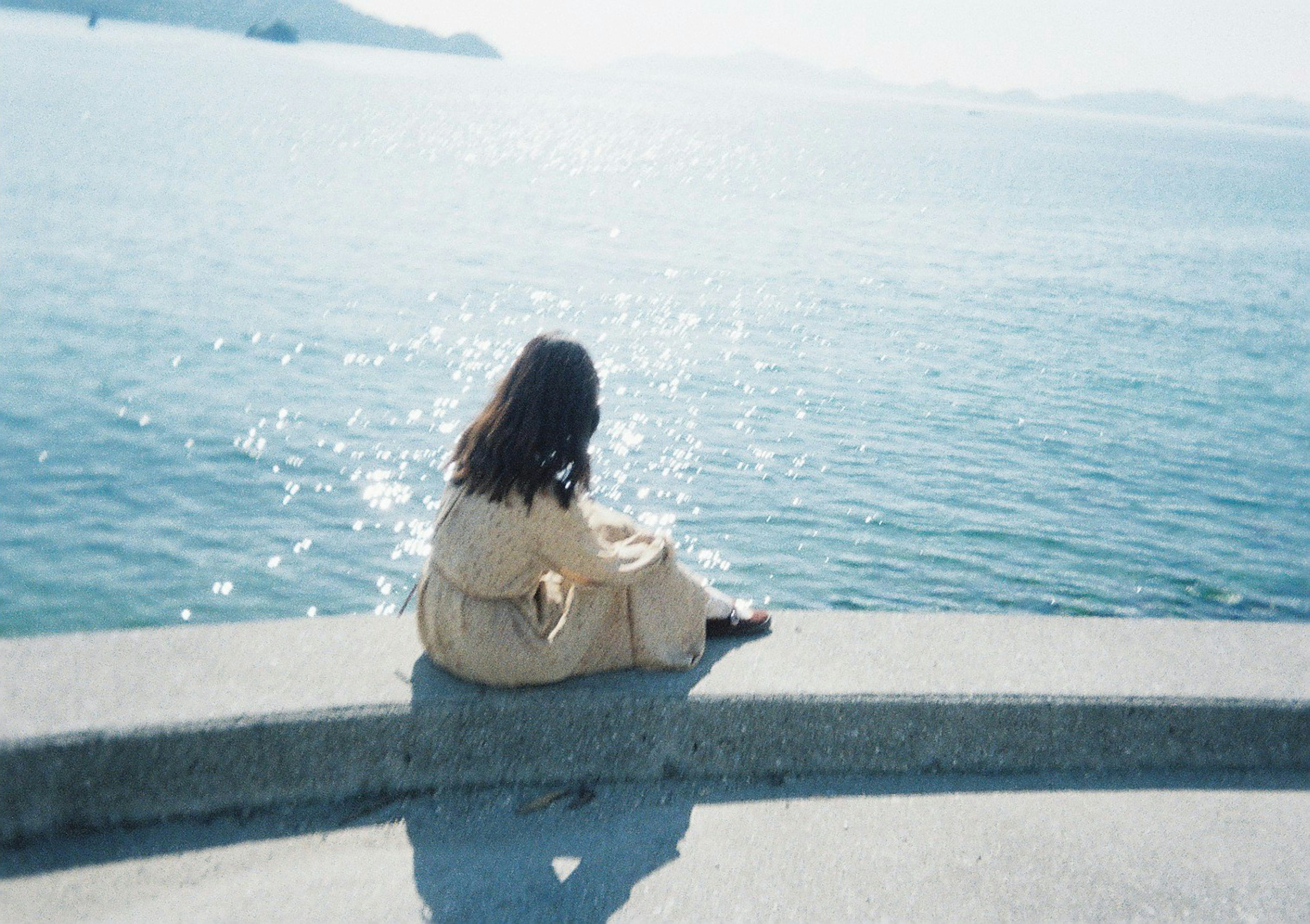 A woman sitting by the sea with her back to the camera