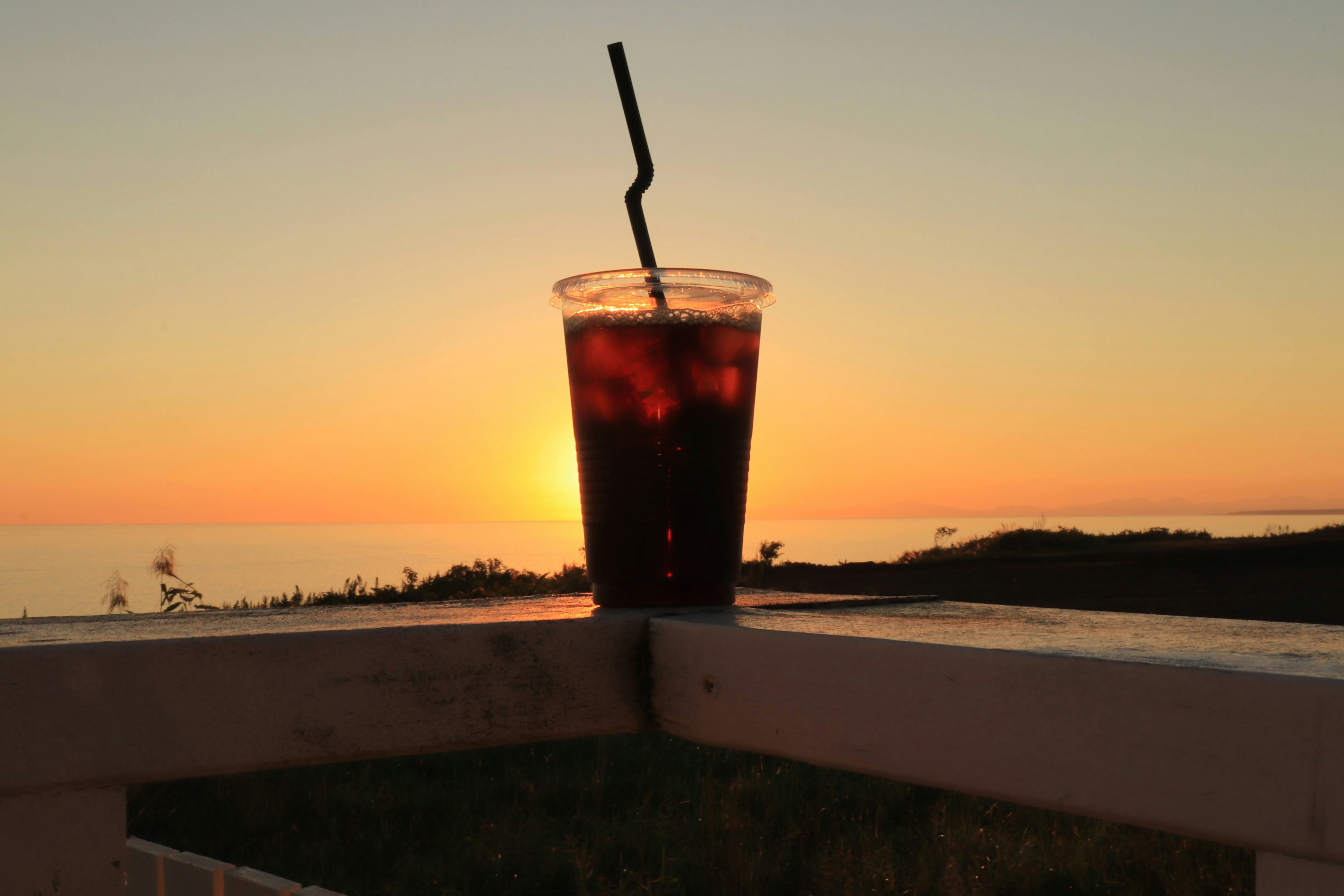 Gelas minuman dingin bersiluet di latar belakang matahari terbenam