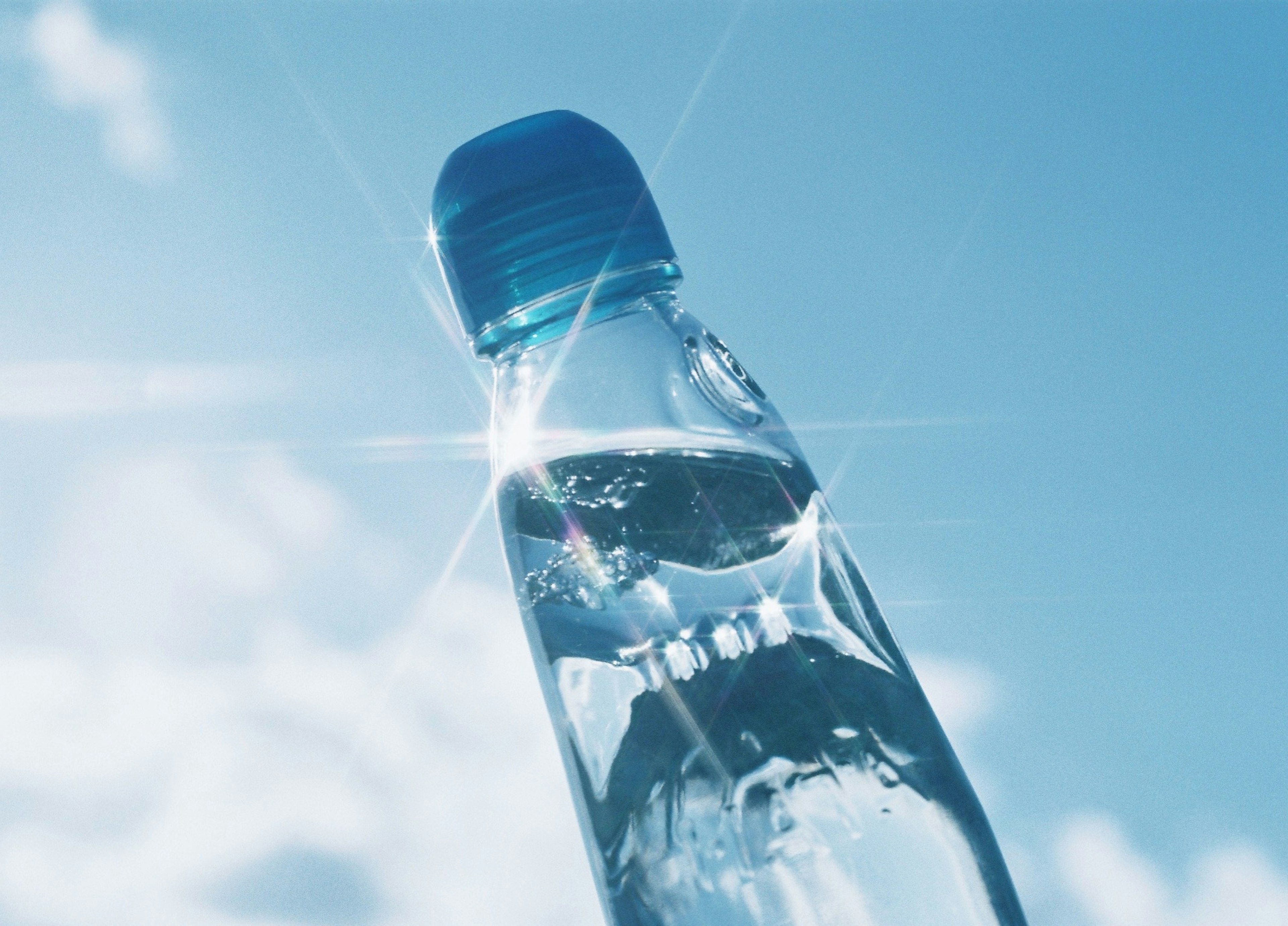 Bottiglia d'acqua che riflette la luce sotto un cielo blu