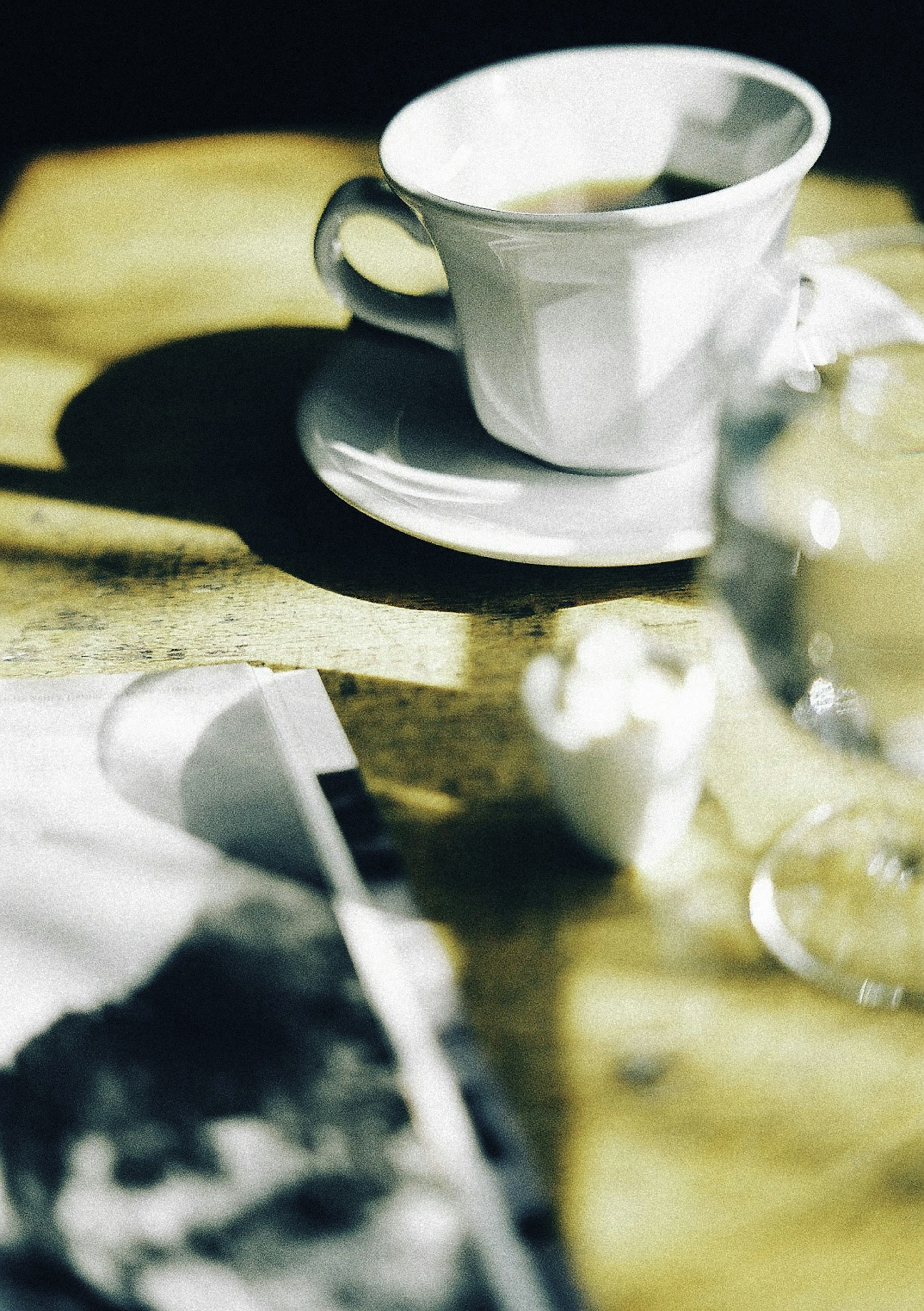 Una tazza di caffè bianca su un piattino con caffè e un bicchiere d'acqua su un tavolo di legno