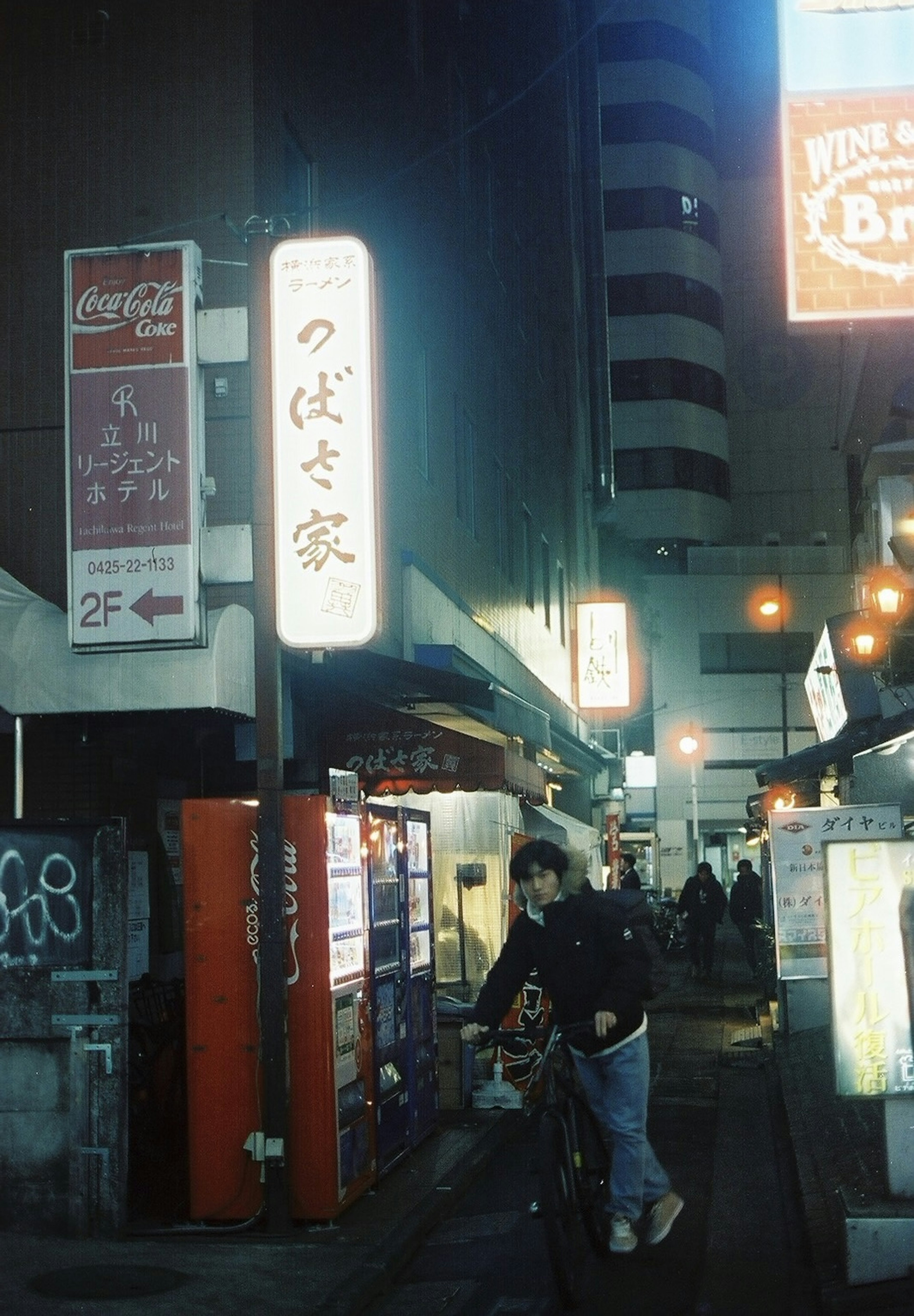 Night street scene featuring a restaurant sign and a person riding a bicycle