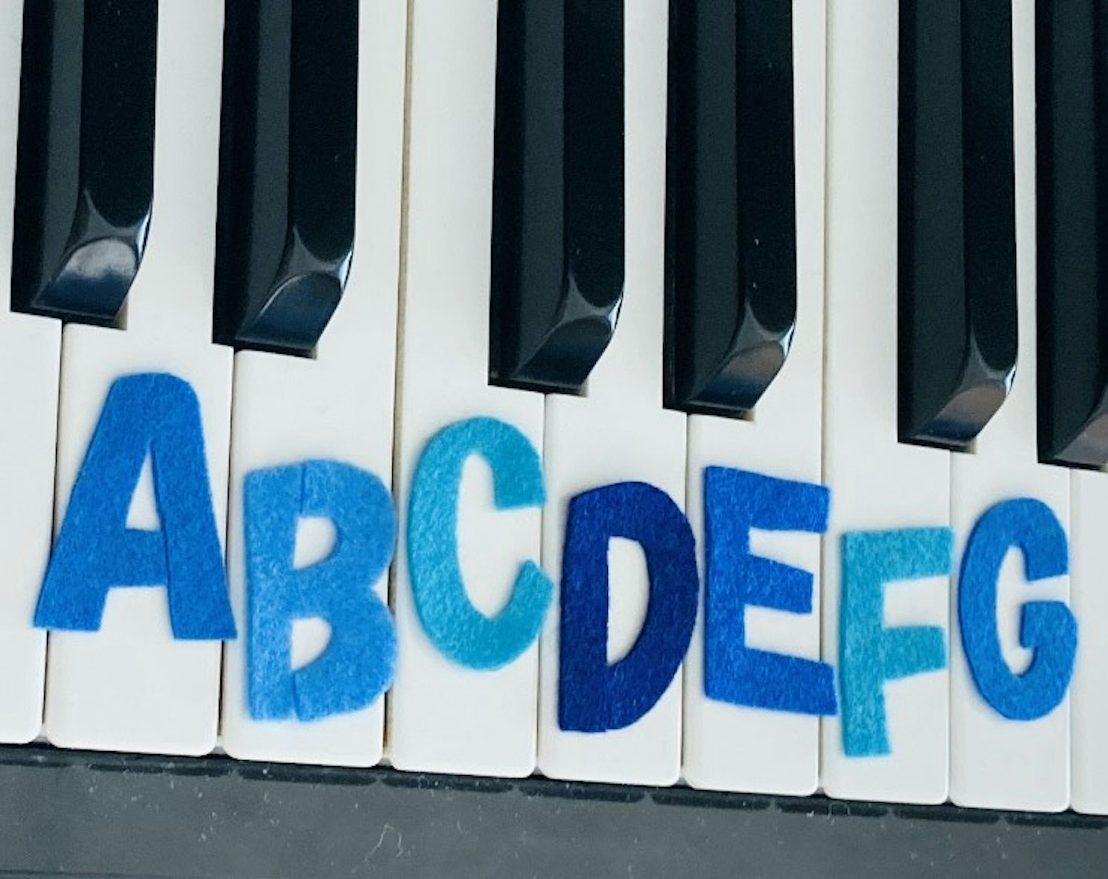 Lettere dell'alfabeto da A a G in feltro blu su tasti di pianoforte