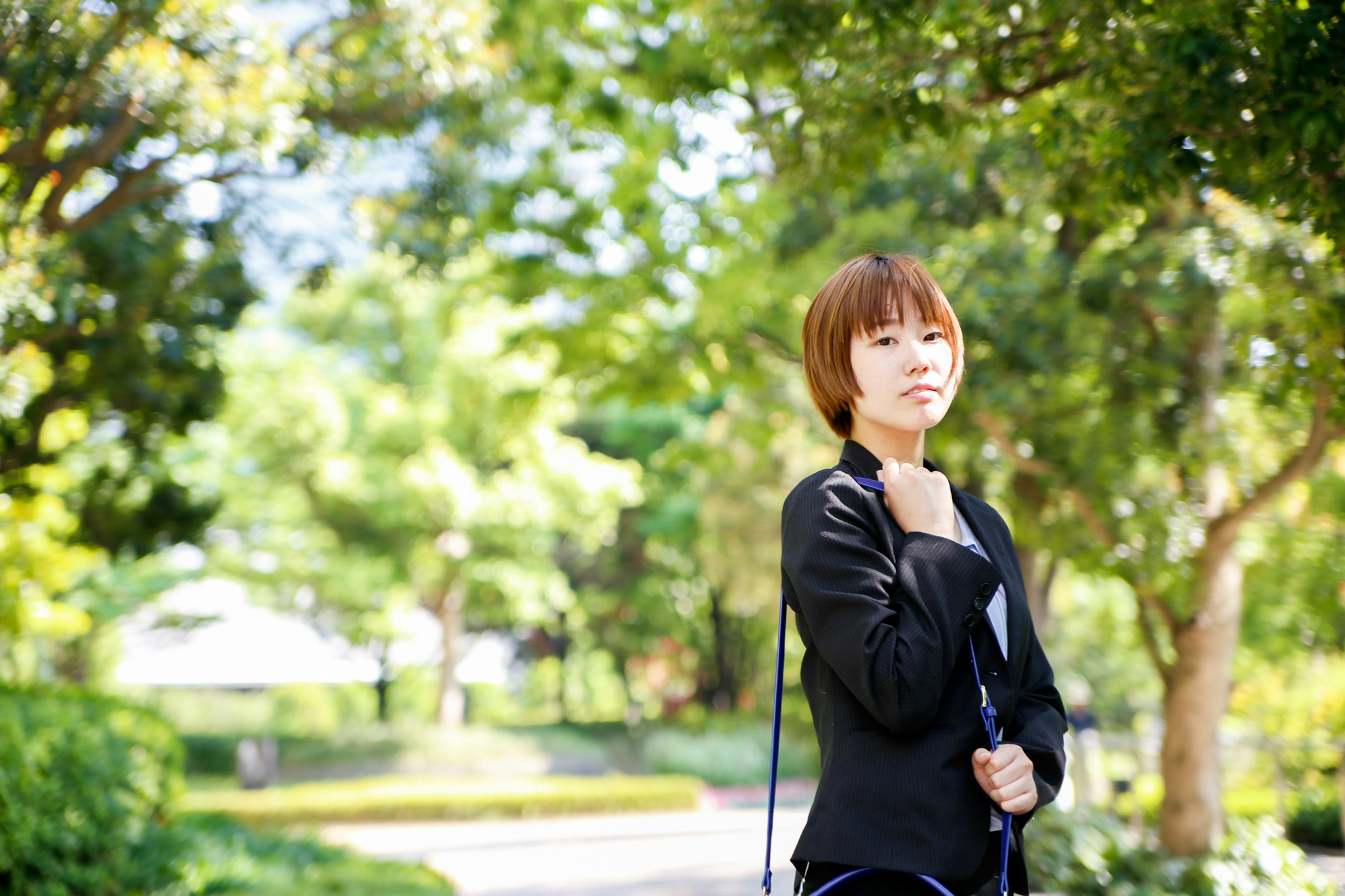 A woman in a black jacket stands in a park