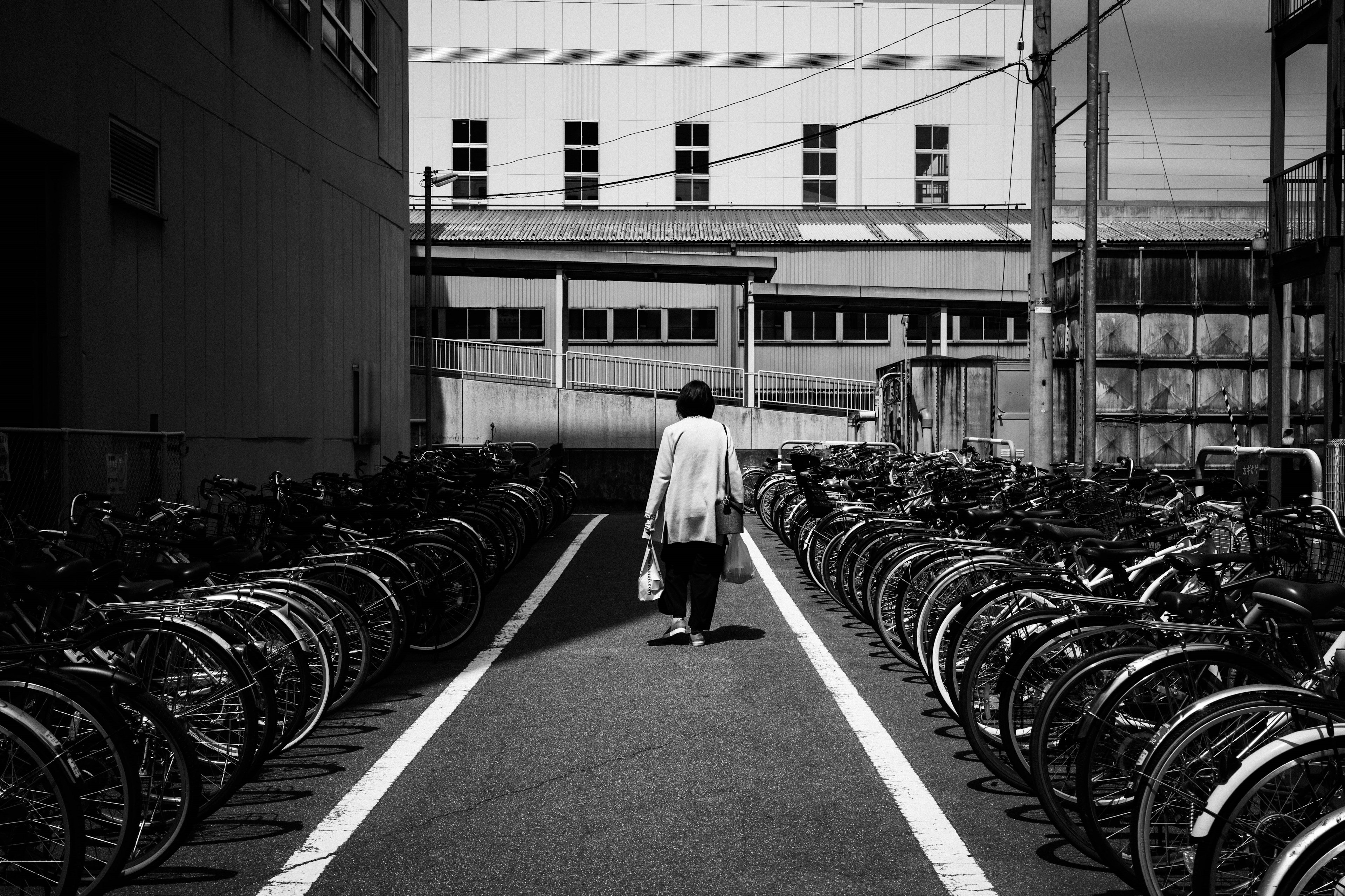 Photo en noir et blanc d'une personne marchant le long d'un chemin bordé de vélos