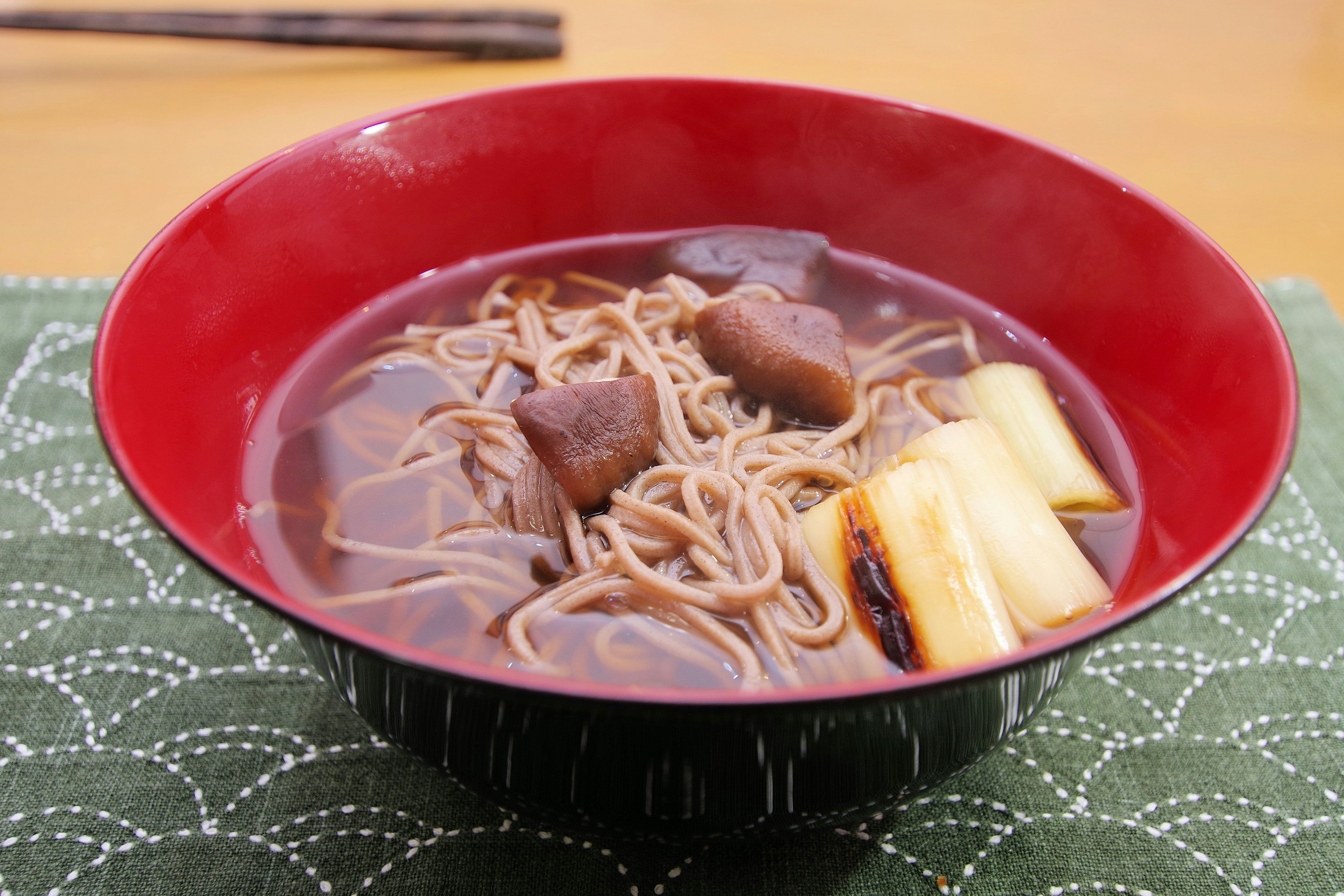 Soba noodles in a red bowl with sweet red bean paste and pieces of daikon