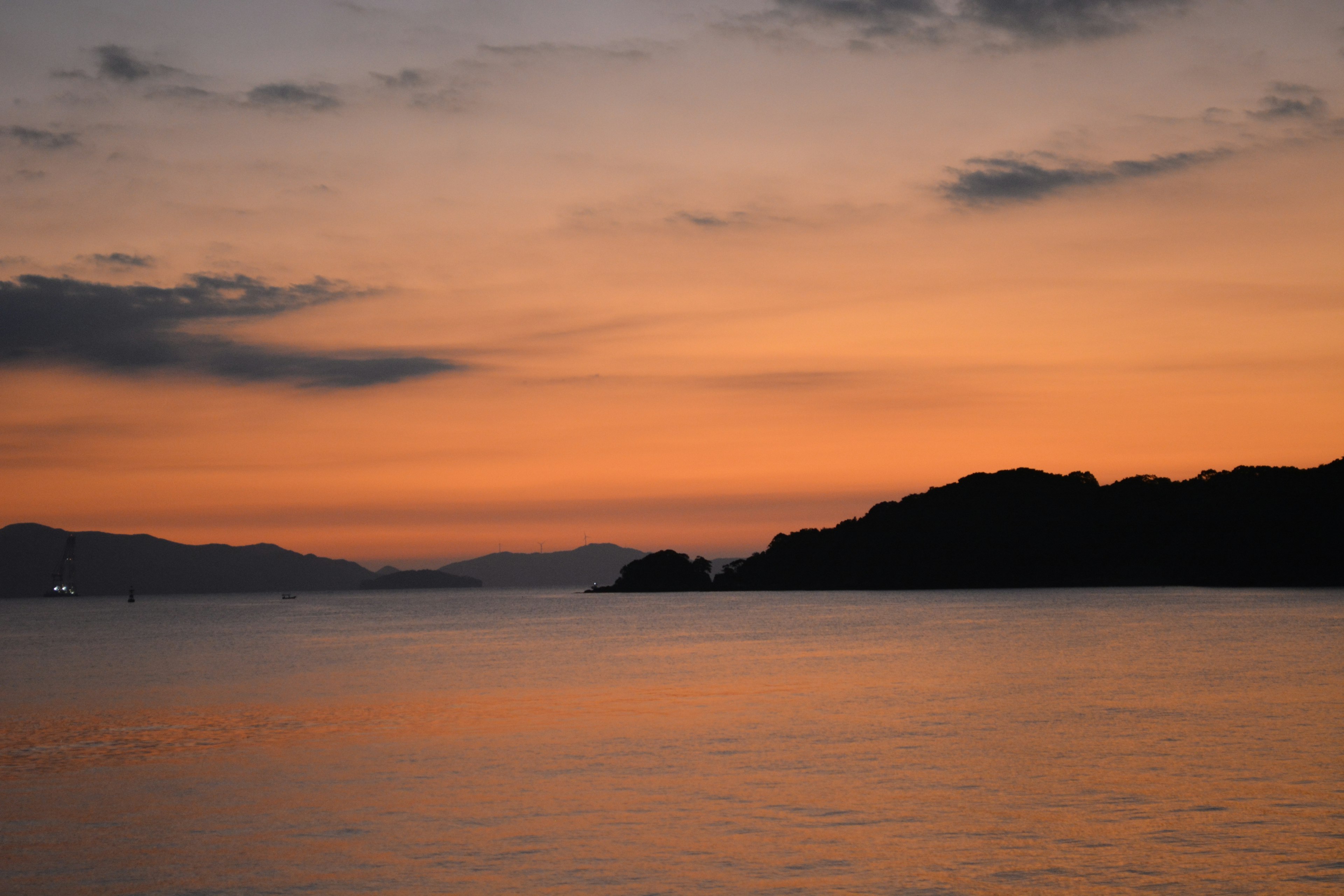 Paesaggio marino sereno con un vivace tramonto arancione e colline in silhouette