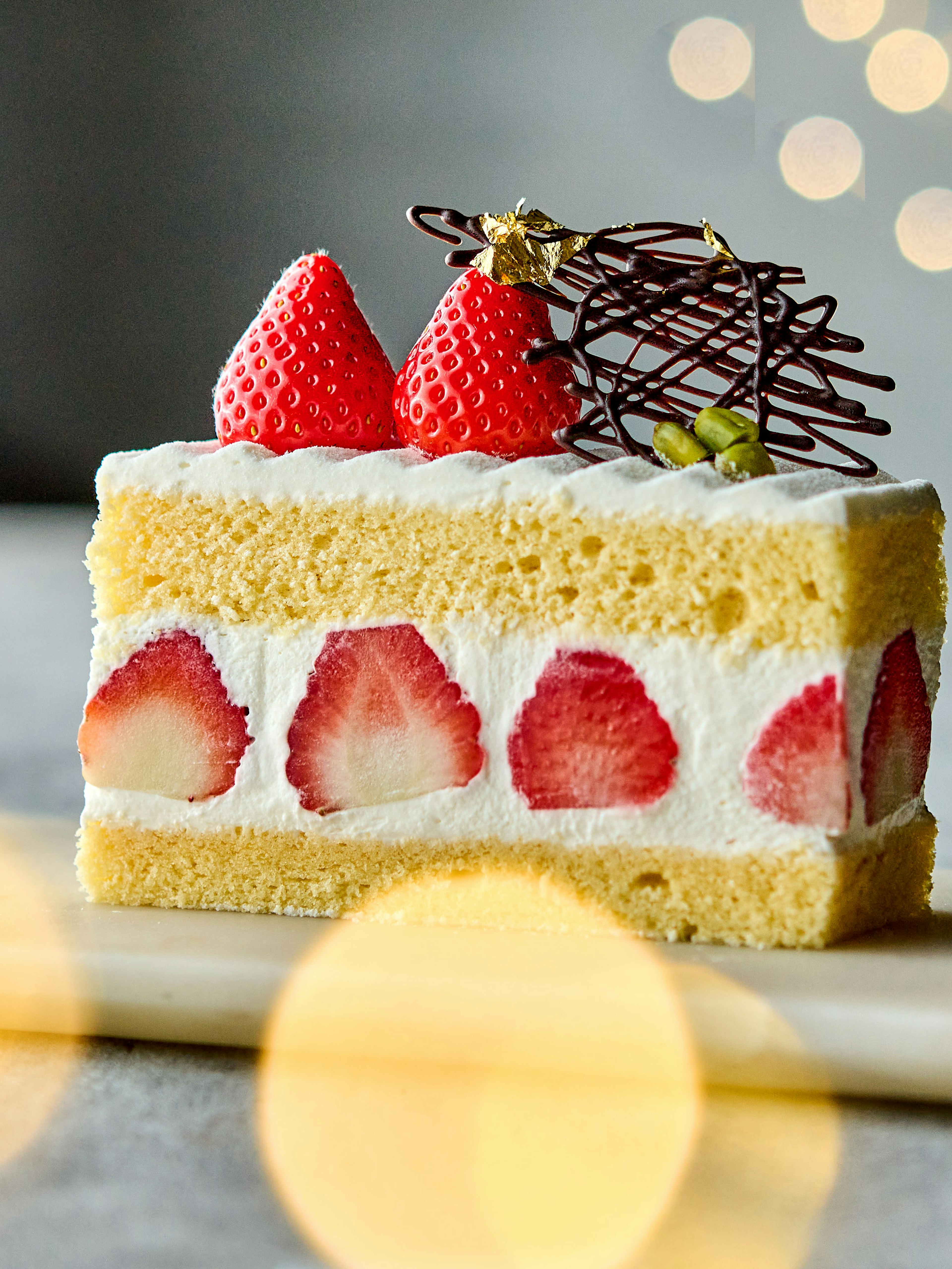 Fetta di torta decorata con fragole e panna guarnita con tre fragole e filigrana di cioccolato