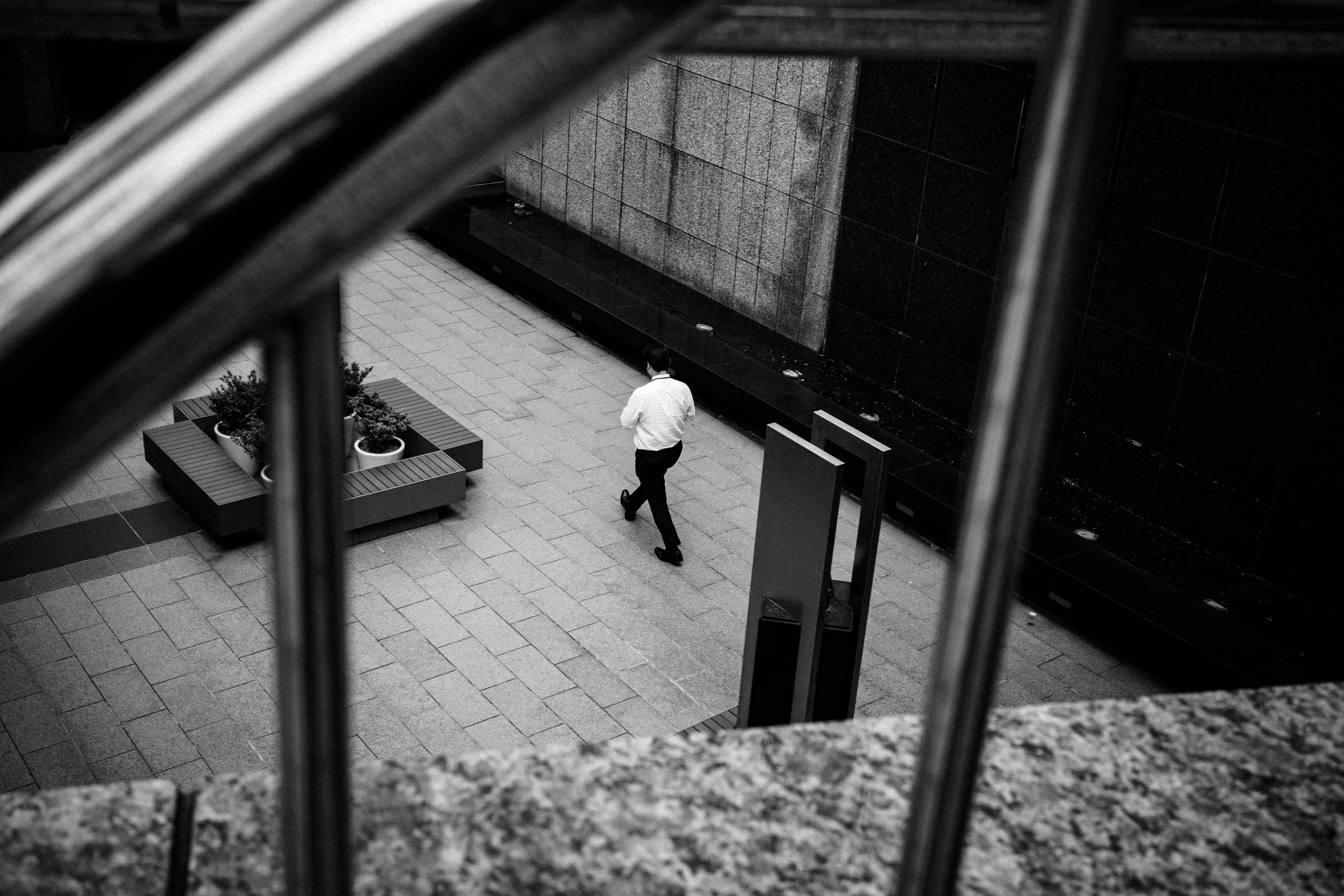 A businessman in a white shirt walking in a monochrome indoor space seen through a railing