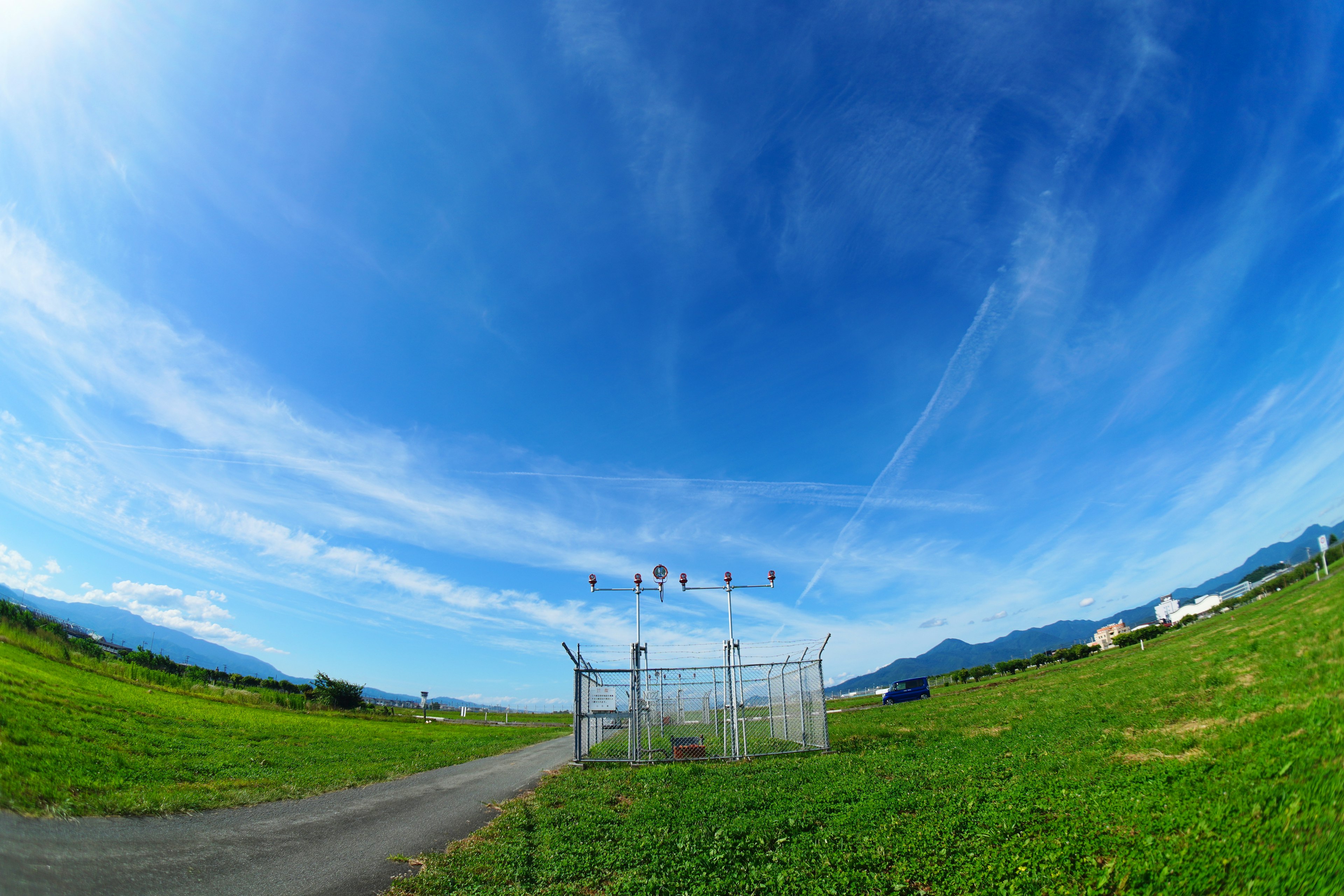 Wide green field under a bright blue sky with a fence in the foreground