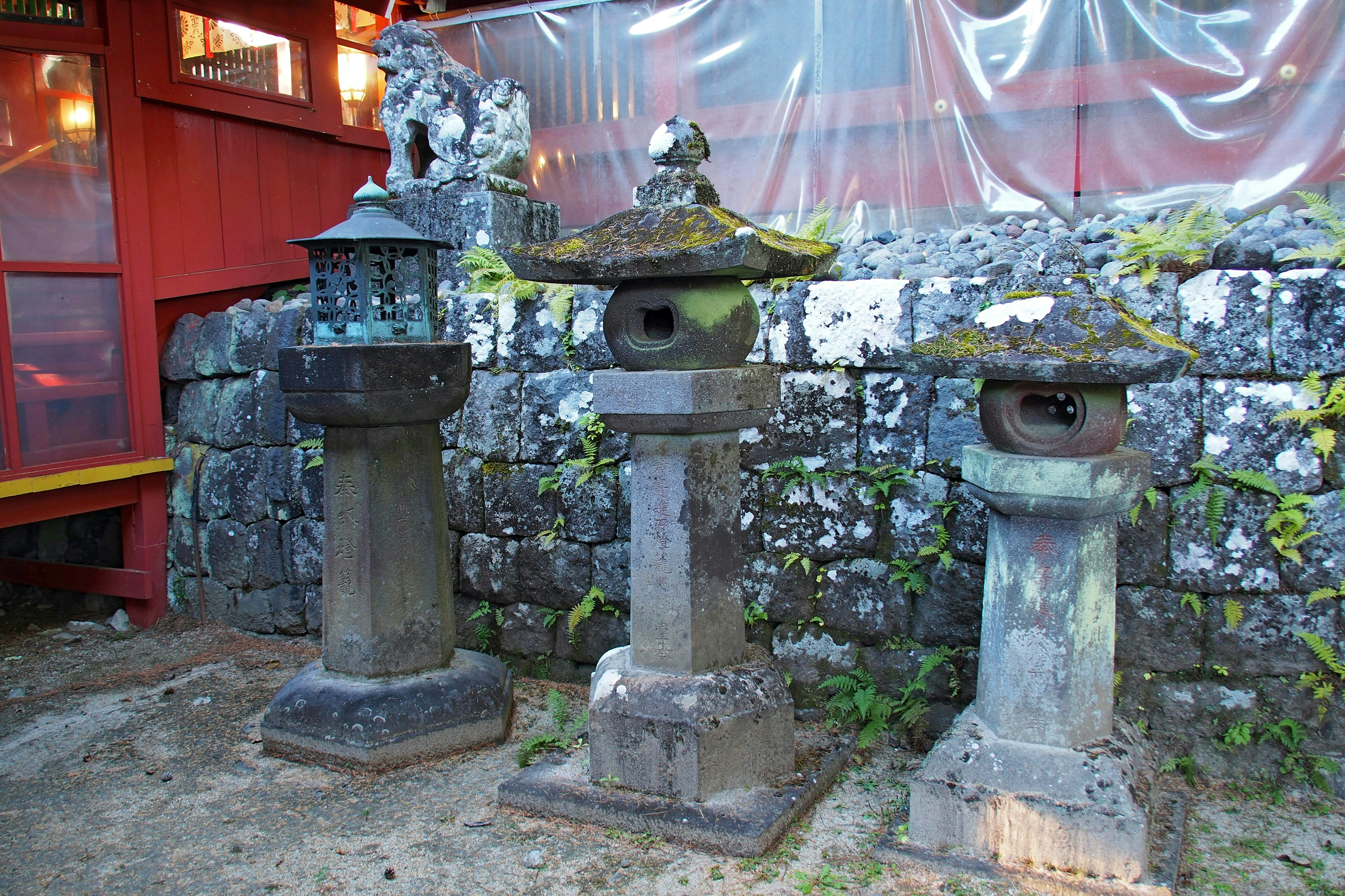 Three traditional stone lanterns in a garden setting moss-covered lanterns with a stone wall background