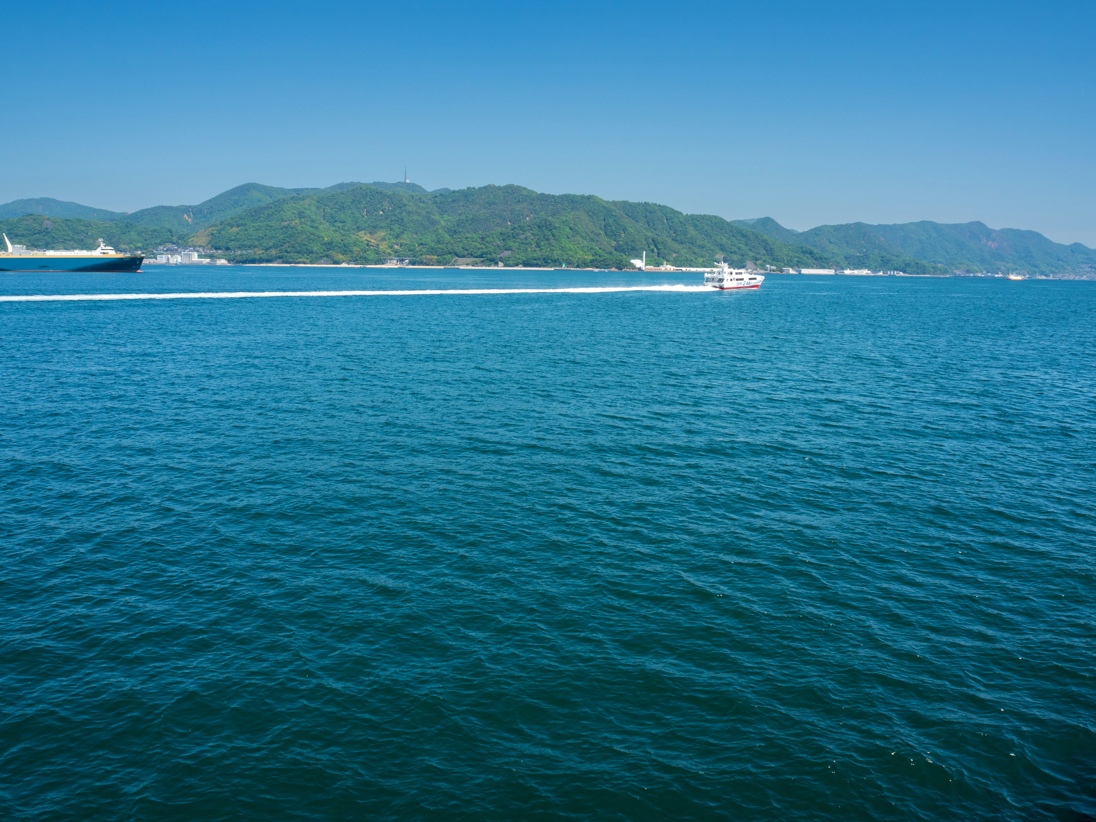 Mar azul claro con montañas verdes al fondo