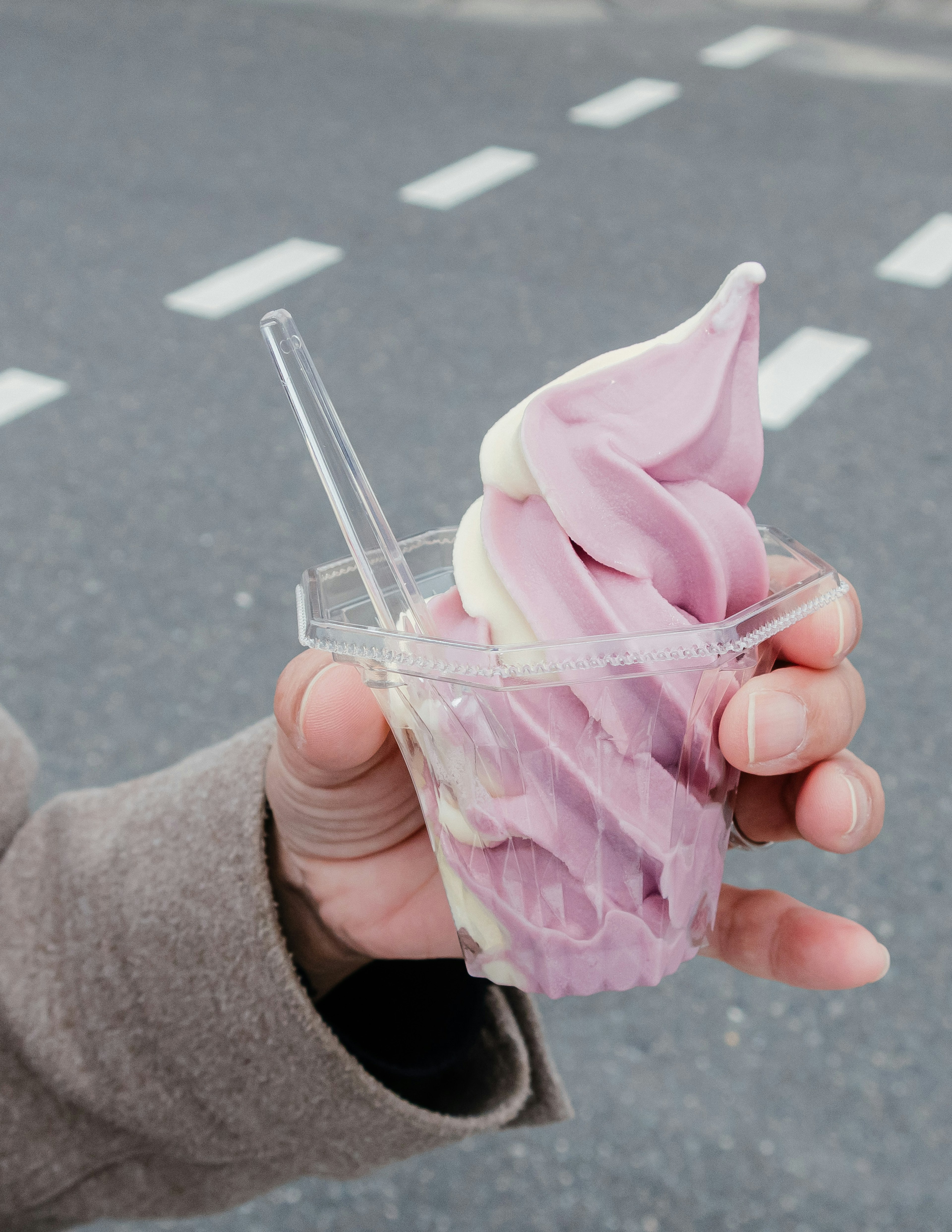 A hand holding a cup of soft serve ice cream with purple swirl