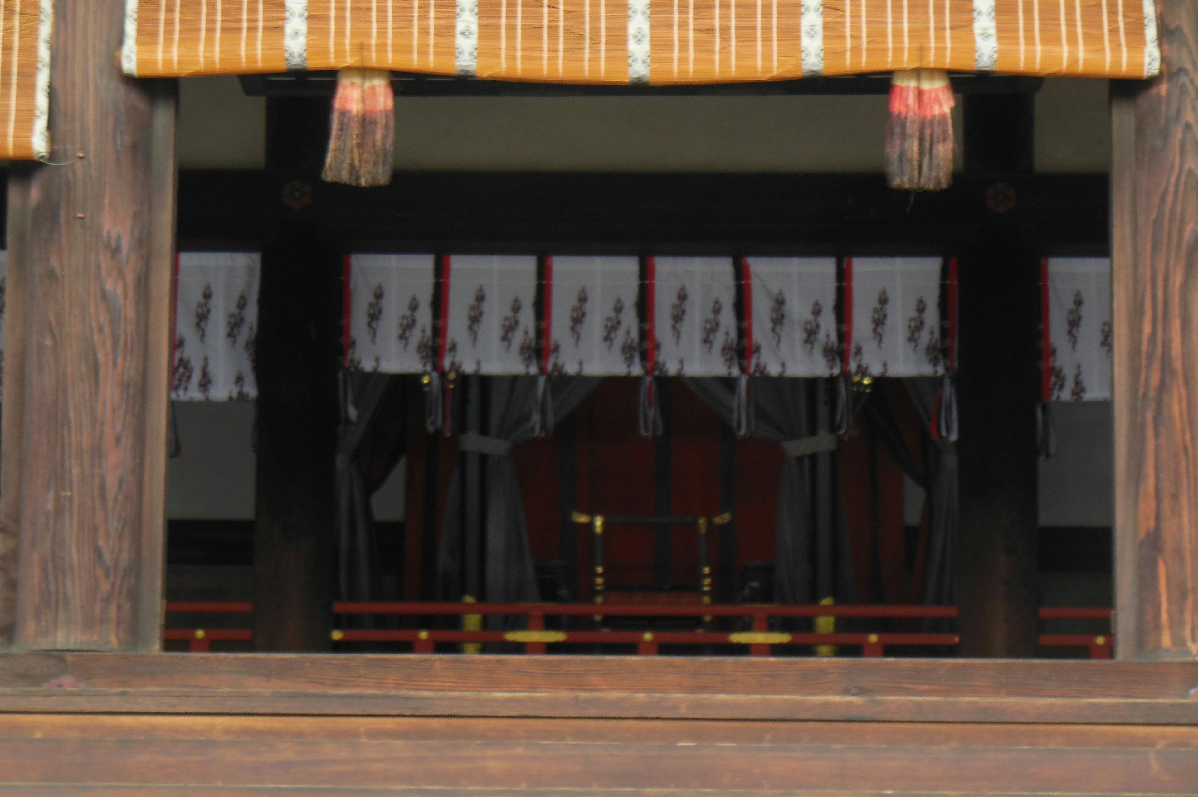 Image of a traditional Japanese shrine interior visible through a window Wooden curtain above the window with sacred decorations inside