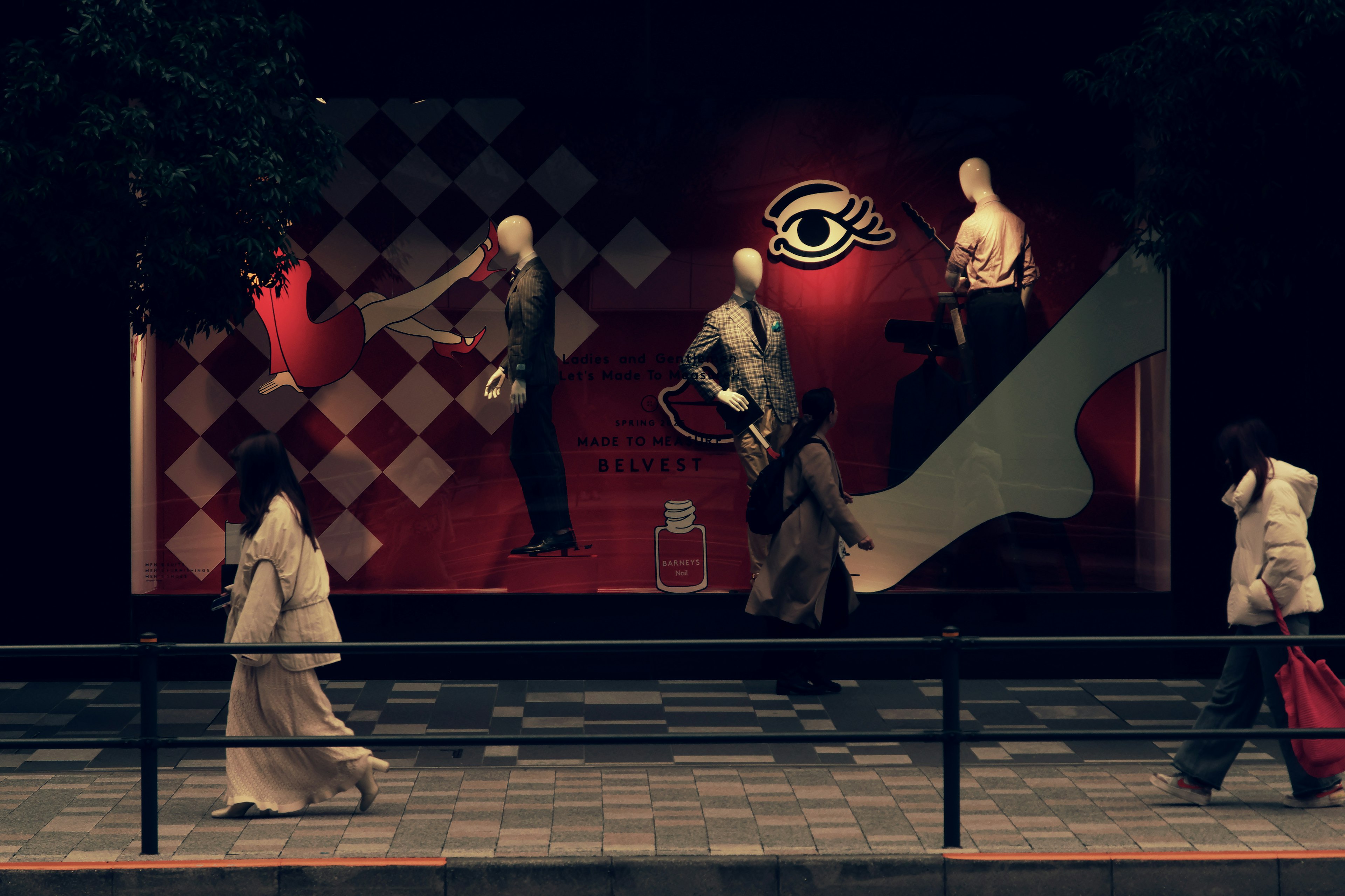 Mannequins displayed in a shop window with pedestrians walking by