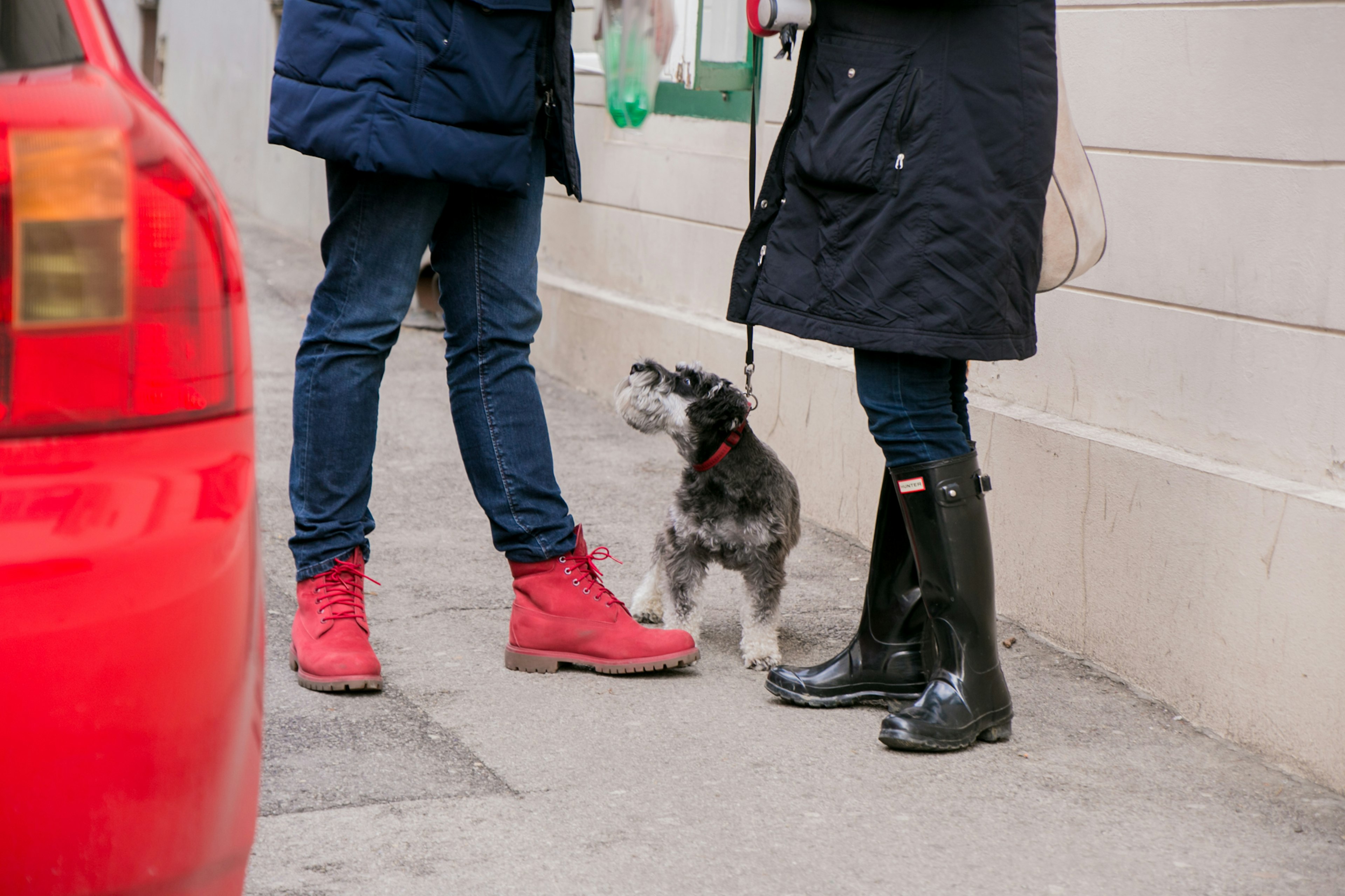 Ein Mann in roten Stiefeln und eine Frau in schwarzen Stiefeln stehen auf der Straße mit einem kleinen Hund zu ihren Füßen