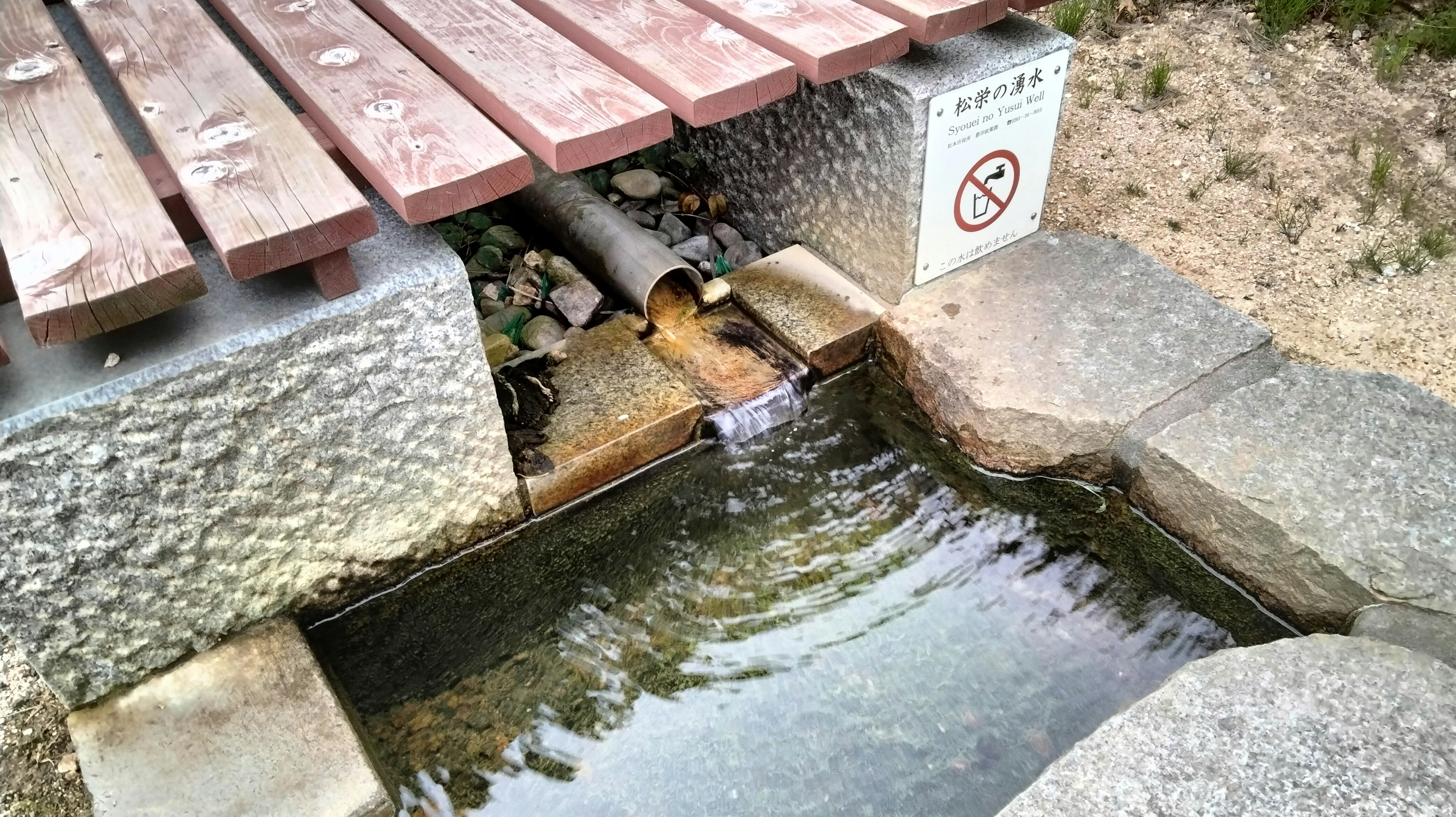 Clear water flowing from a pipe under a wooden bench with a stone border