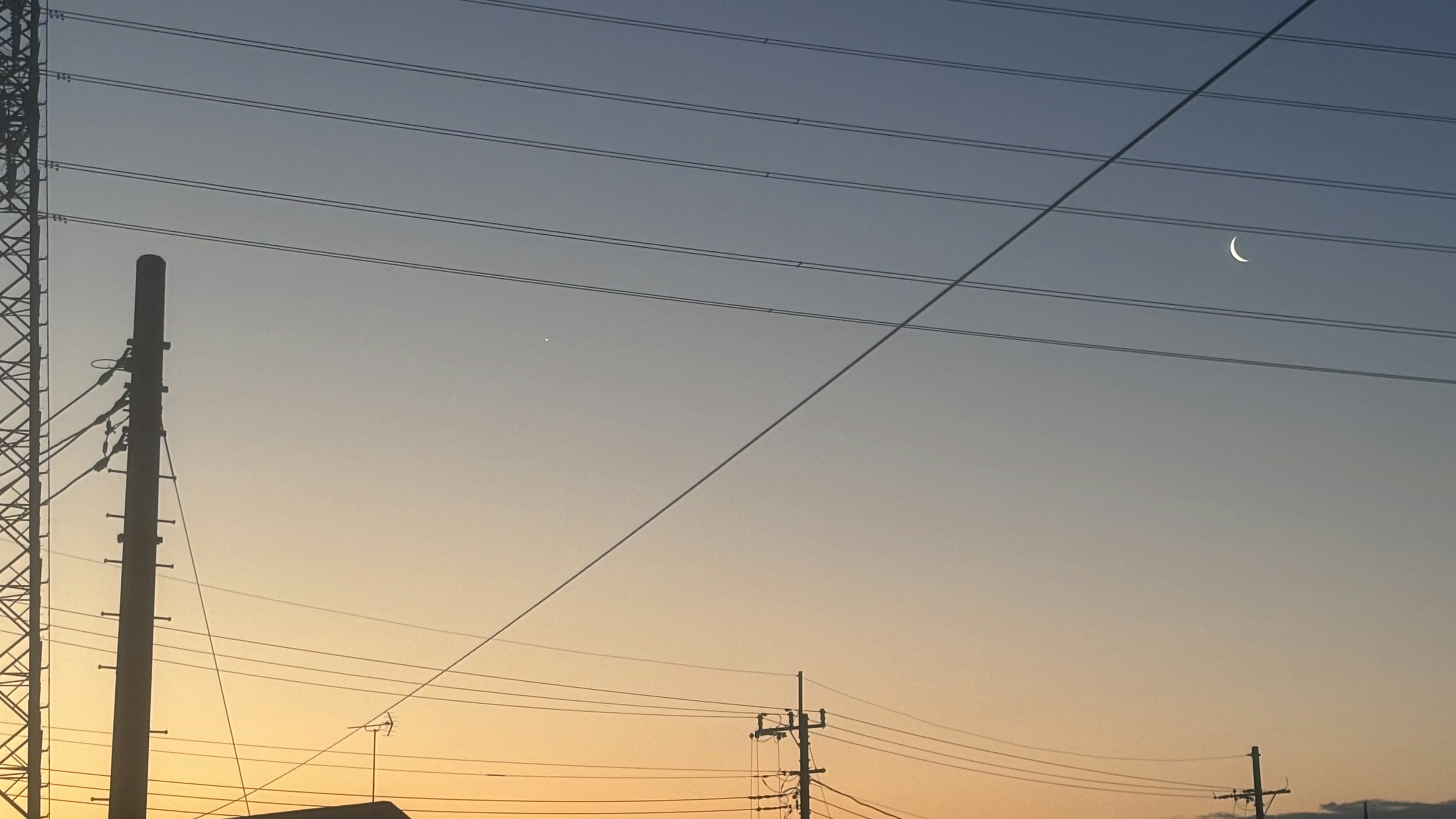 Ciel crépusculaire avec une lune croissante et des lignes électriques