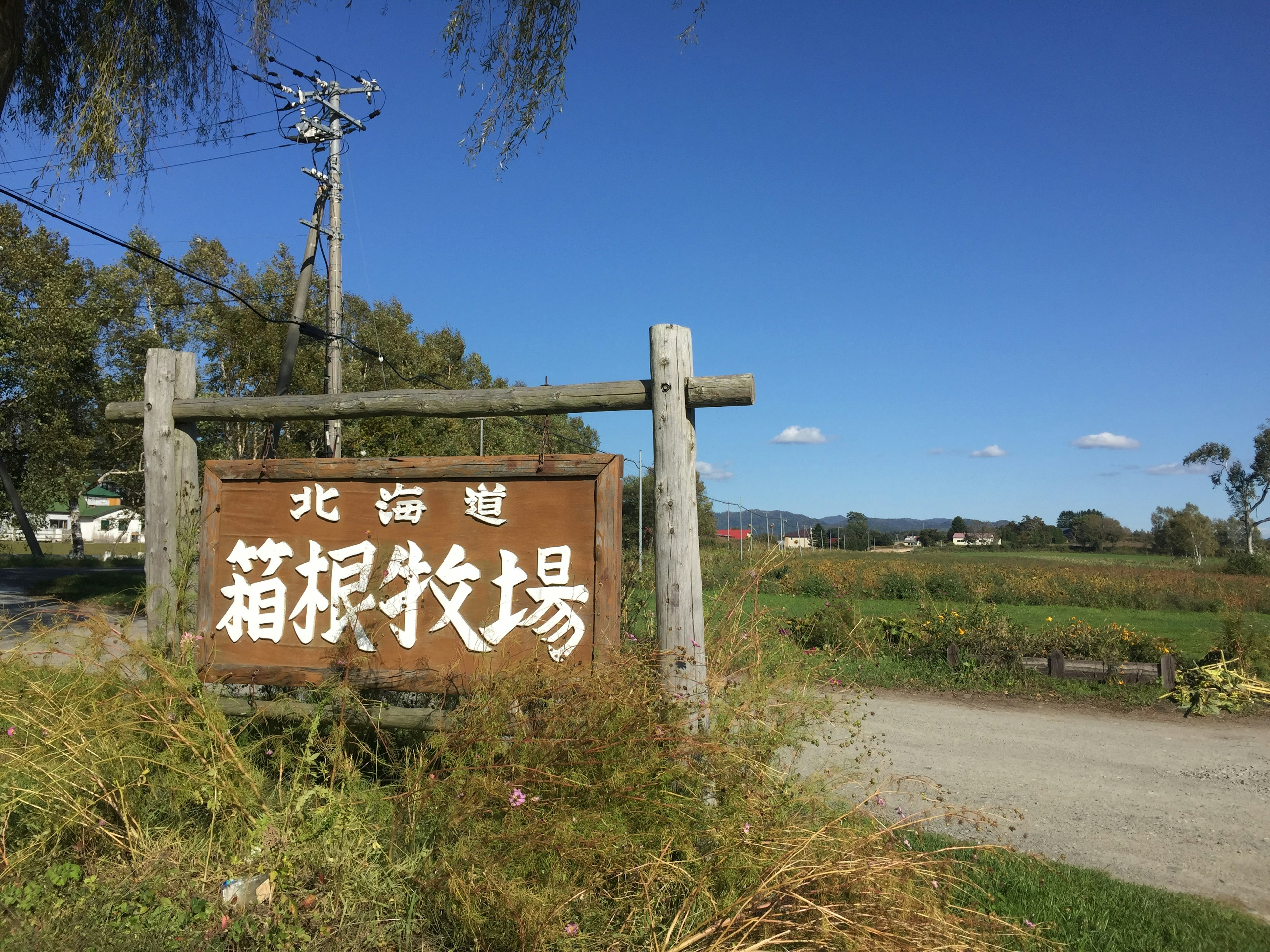 Cartello in legno sotto un cielo blu con paesaggio agricolo