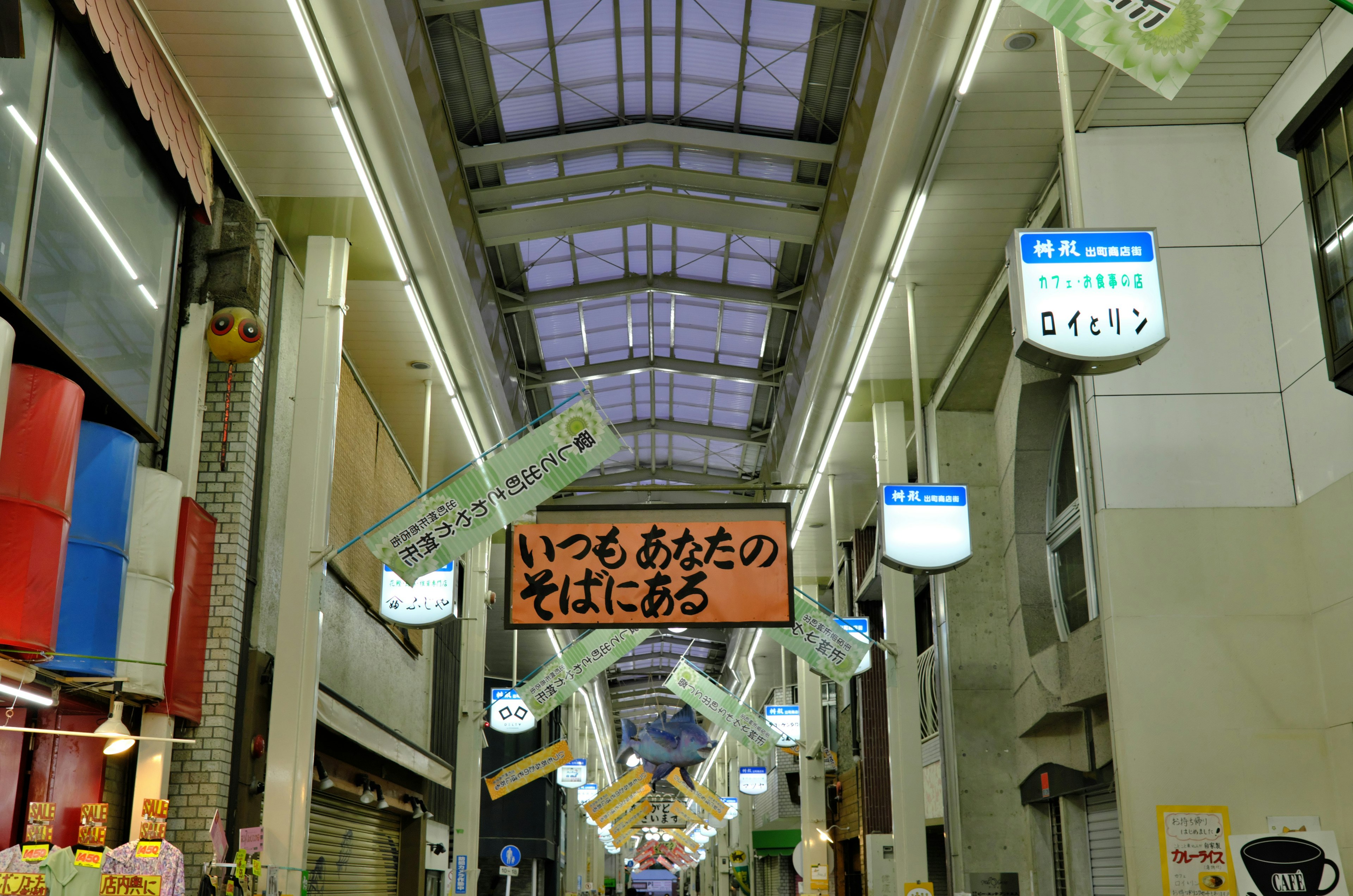 Scena di strada luminosa sotto il tetto di un'arcade commerciale con insegne appese e illuminazione