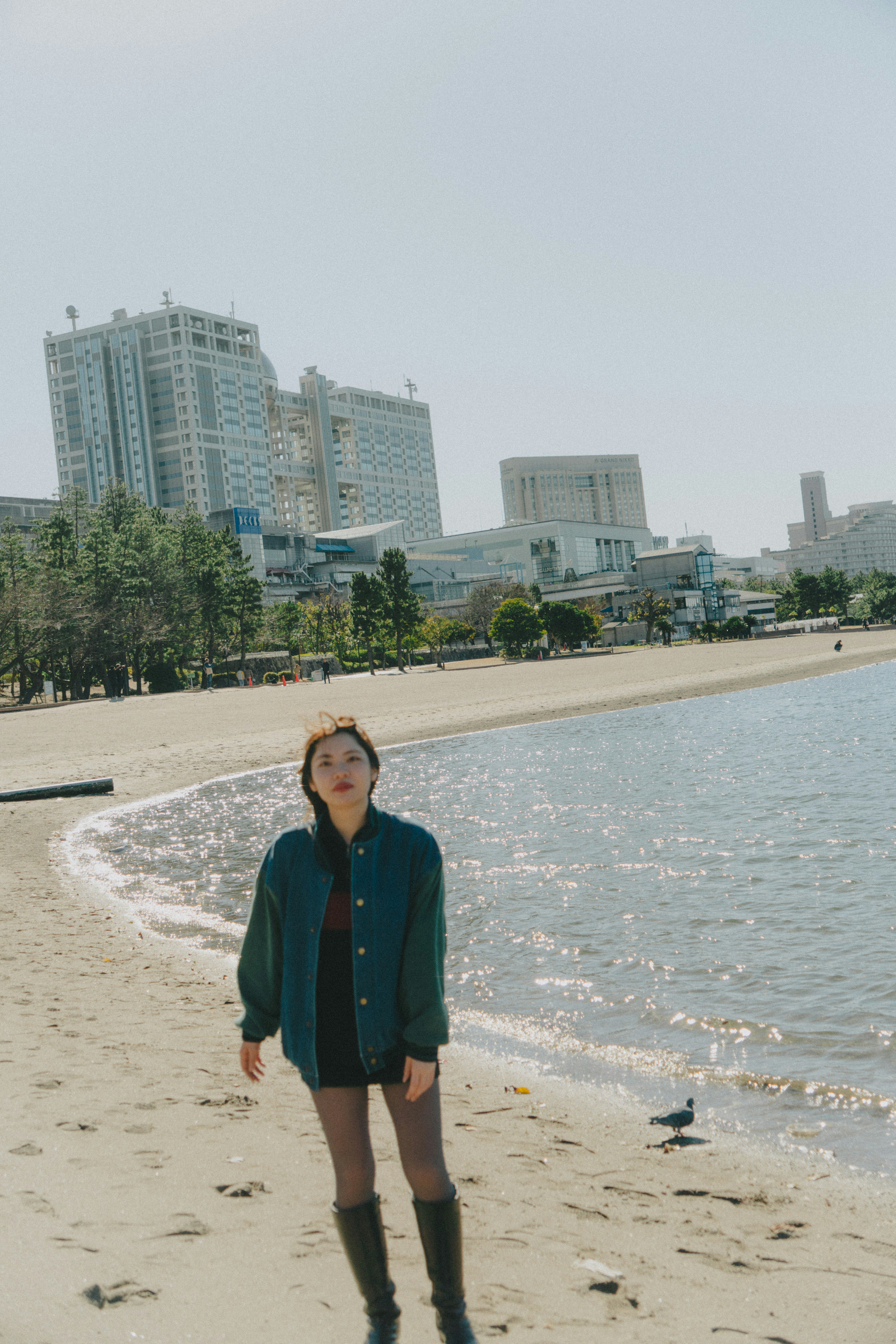 Wanita berpose di pantai dengan gedung tinggi di latar belakang