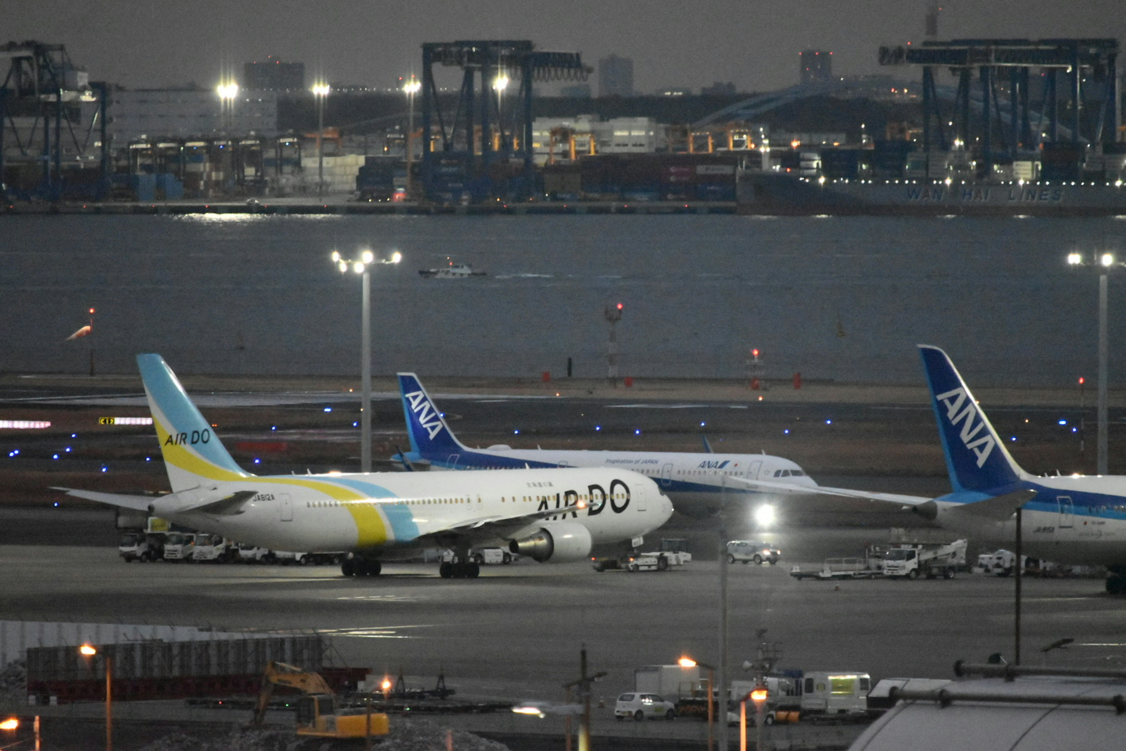 Aviones aparcados en un aeropuerto durante el crepúsculo con luces del puerto de fondo