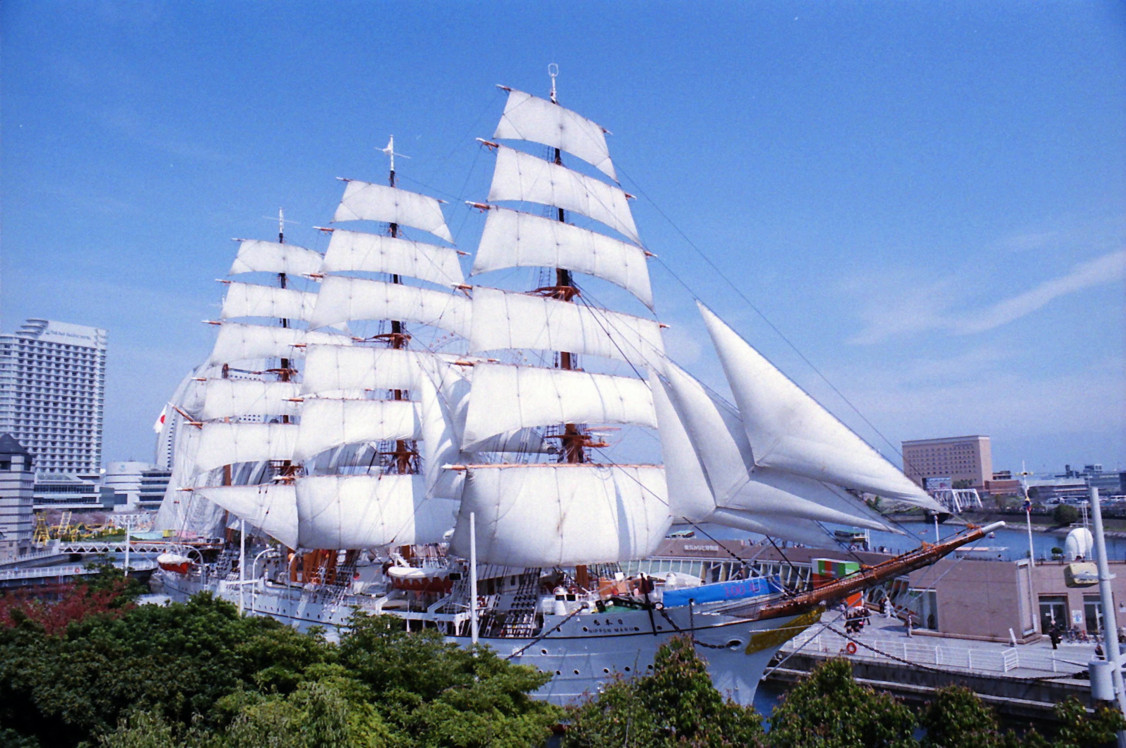 A large sailing ship docked in Yokohama harbor with big white sails billowing in the wind