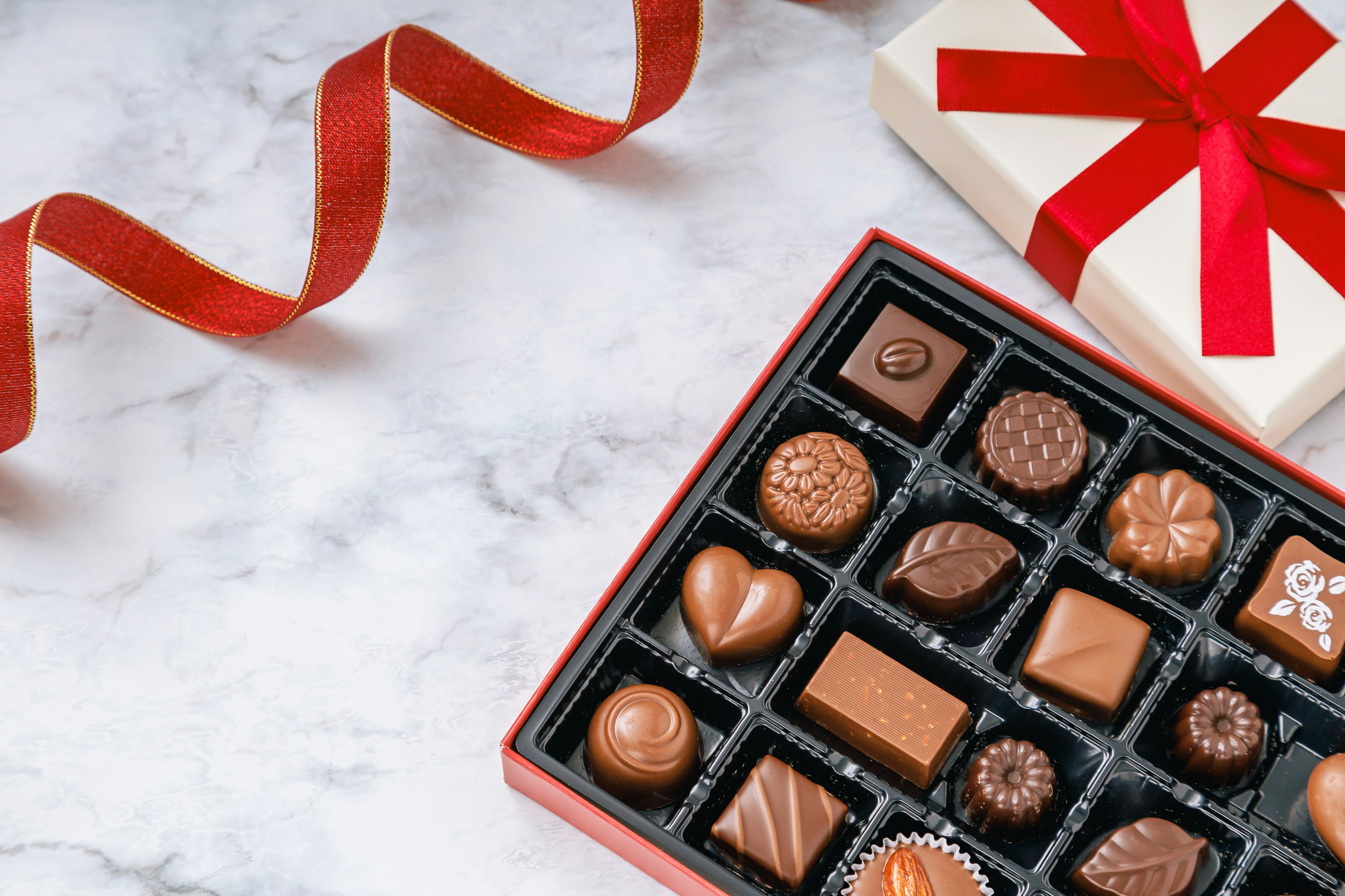 Boîte cadeau avec un ruban rouge et des chocolats assortis dans une boîte