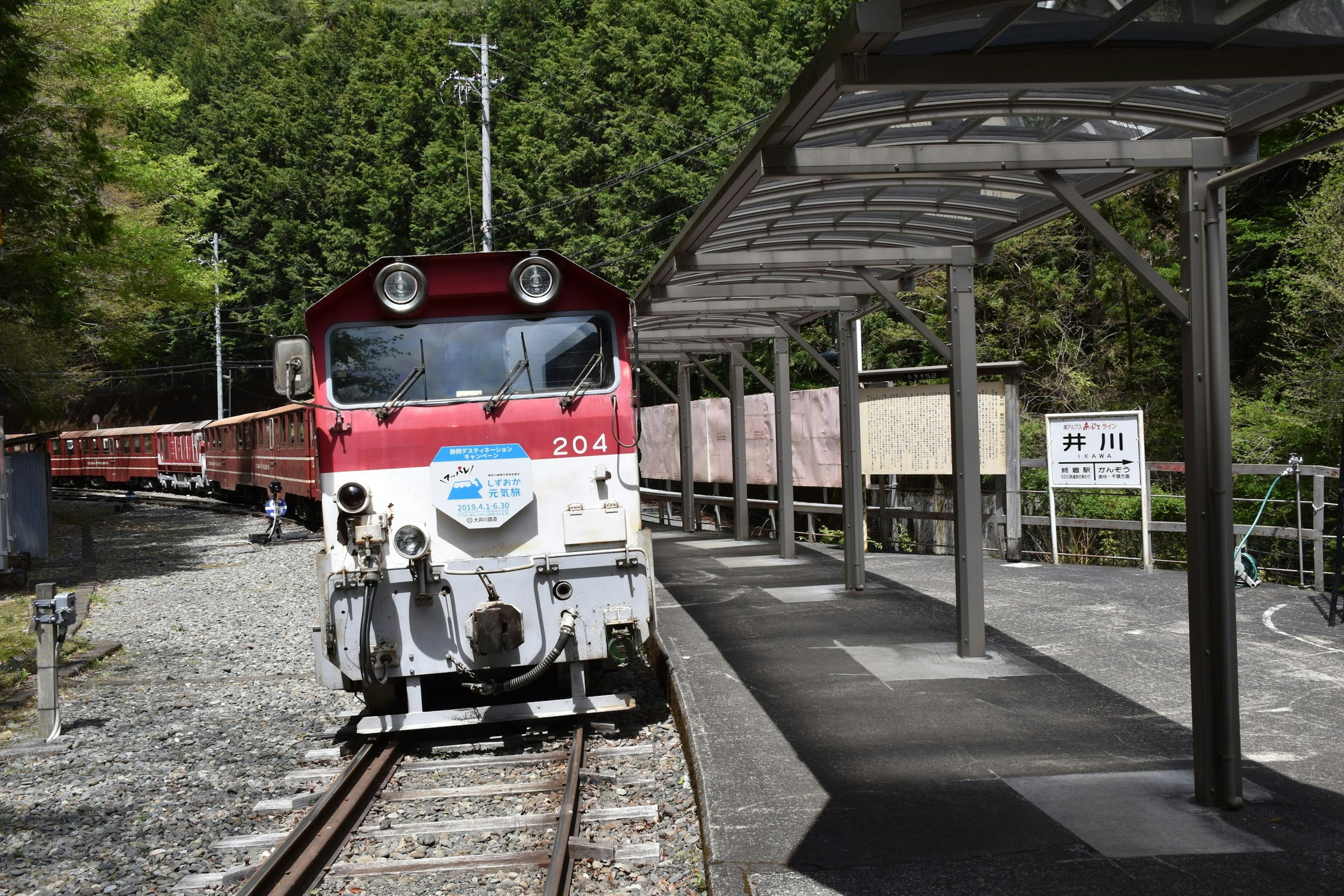 Lokomotif merah di stasiun kereta dengan pohon hijau di latar belakang