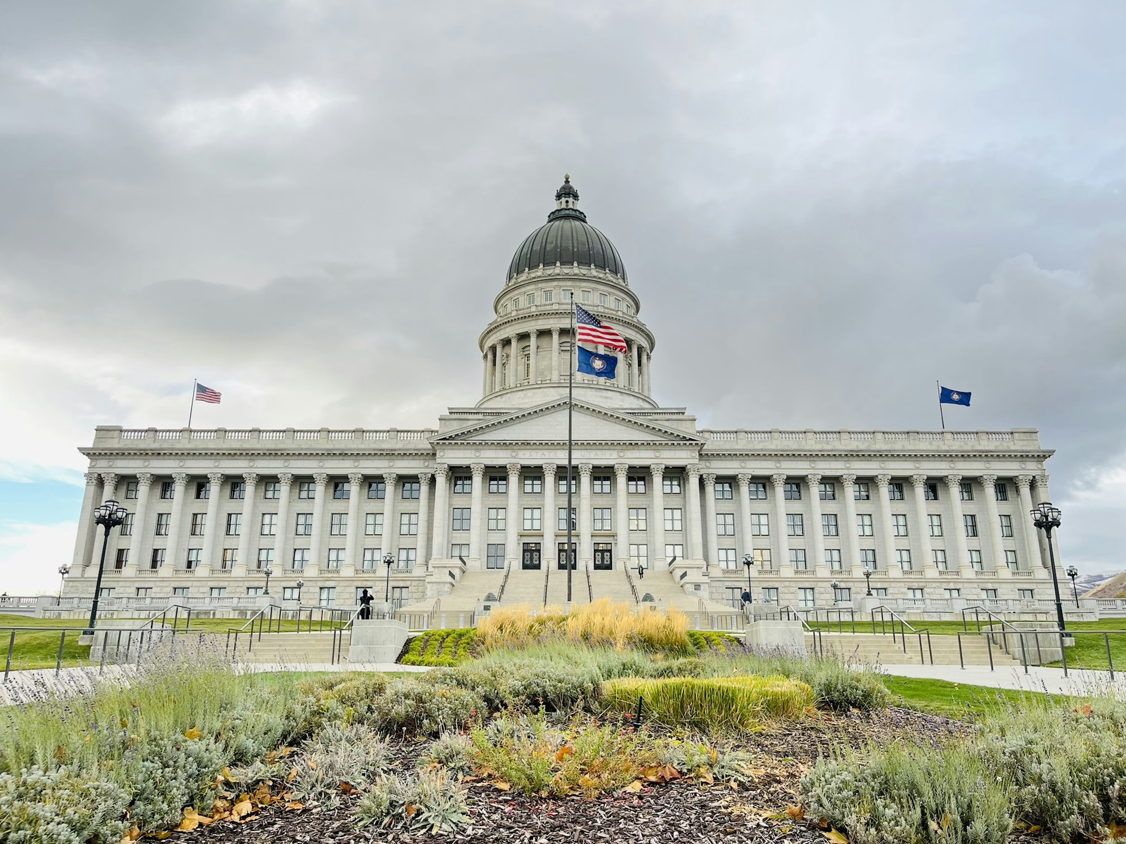 Vista frontal del edificio del Capitolio del Estado de Utah con cielo nublado y vegetación en primer plano