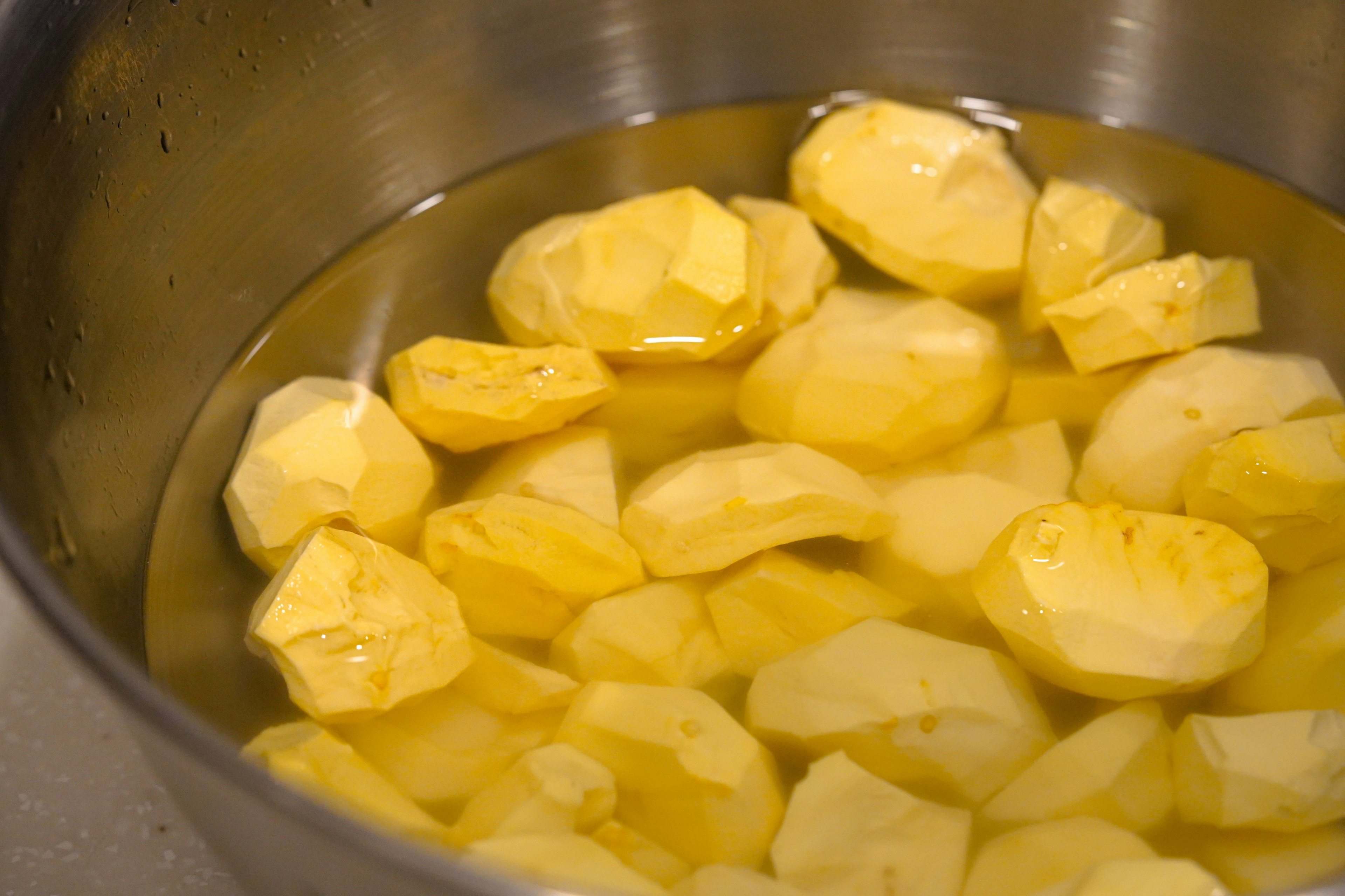 Peeled potatoes submerged in water in a stainless steel bowl