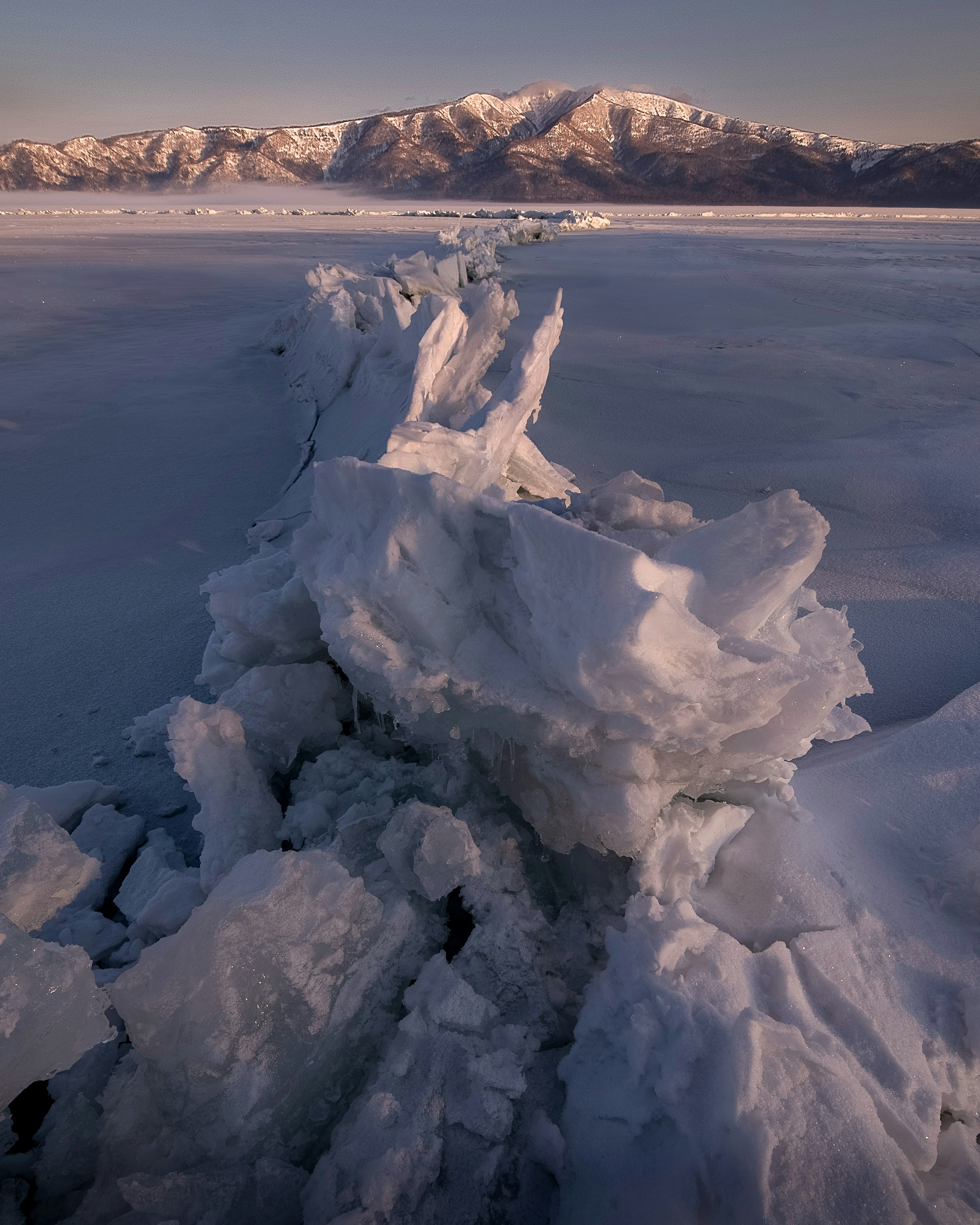 Paesaggio invernale con formazioni di ghiaccio e montagne sullo sfondo